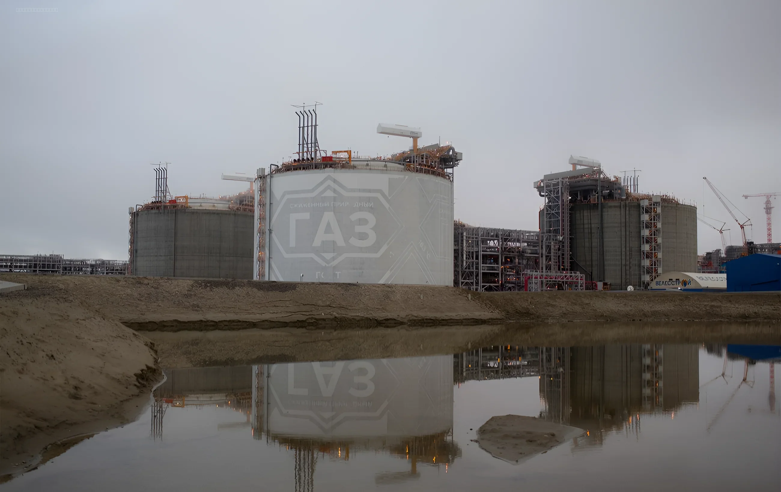 Крупные газовые резервуары на фоне пасмурного неба, отражающиеся в воде, иллюстрирующие тему энергетического давления России на Армению