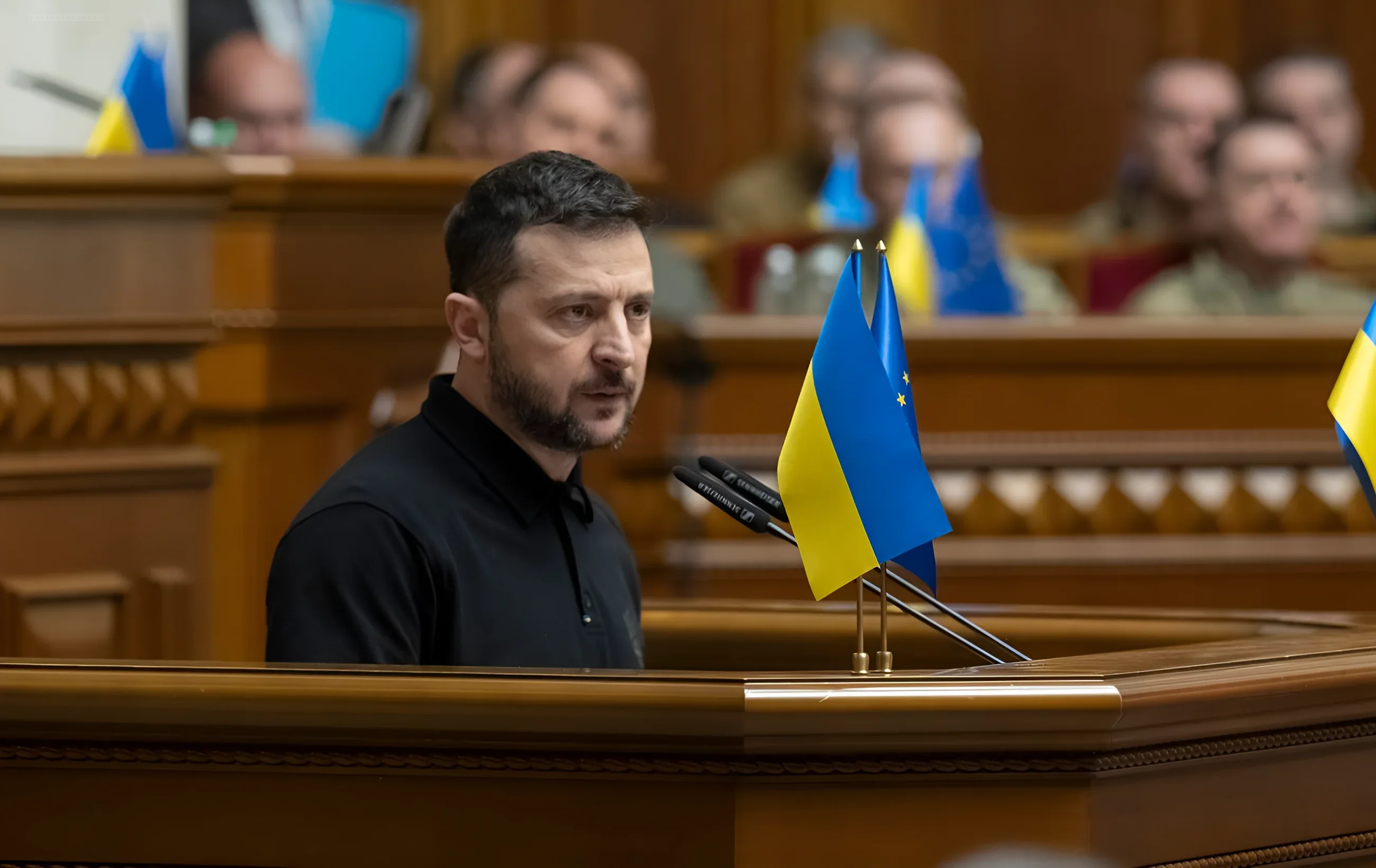 Volodymyr Zelenskyy delivering a speech in the Verkhovna Rada of Ukraine, with flags of Ukraine and the EU on the podium