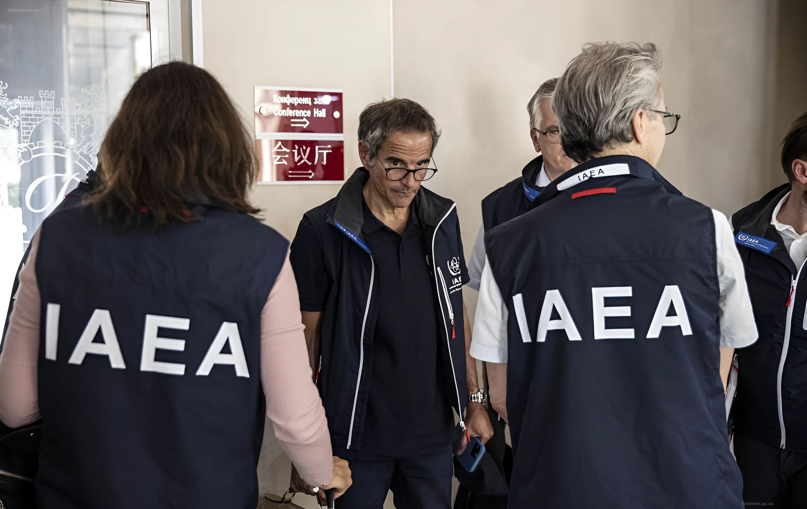 A group of IAEA experts in branded vests discussing the situation in the corridor of a building at the Zaporizhzhia NPP