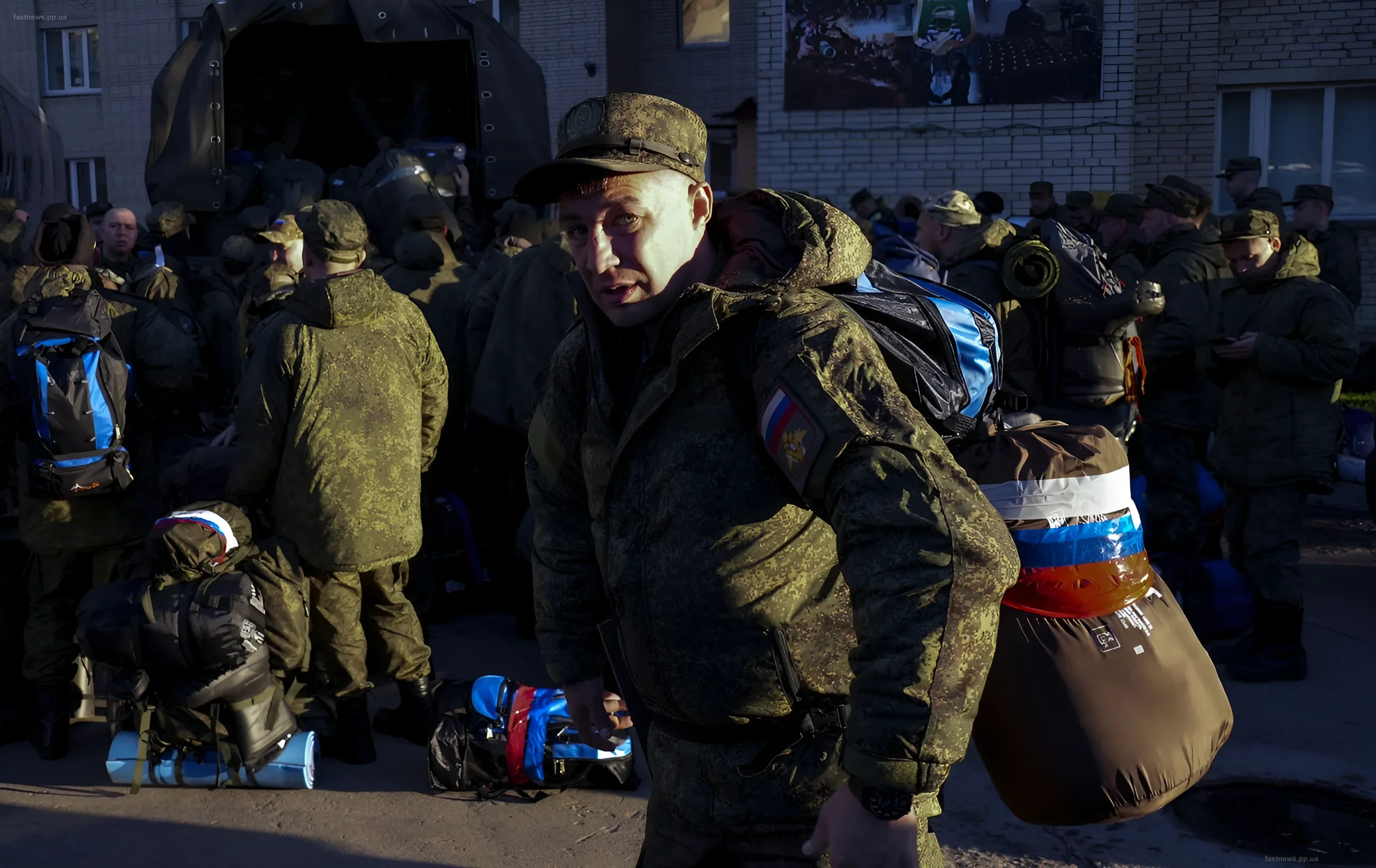 Russian soldiers with backpacks and a Russian flag in front of a building, preparing for deployment to the front