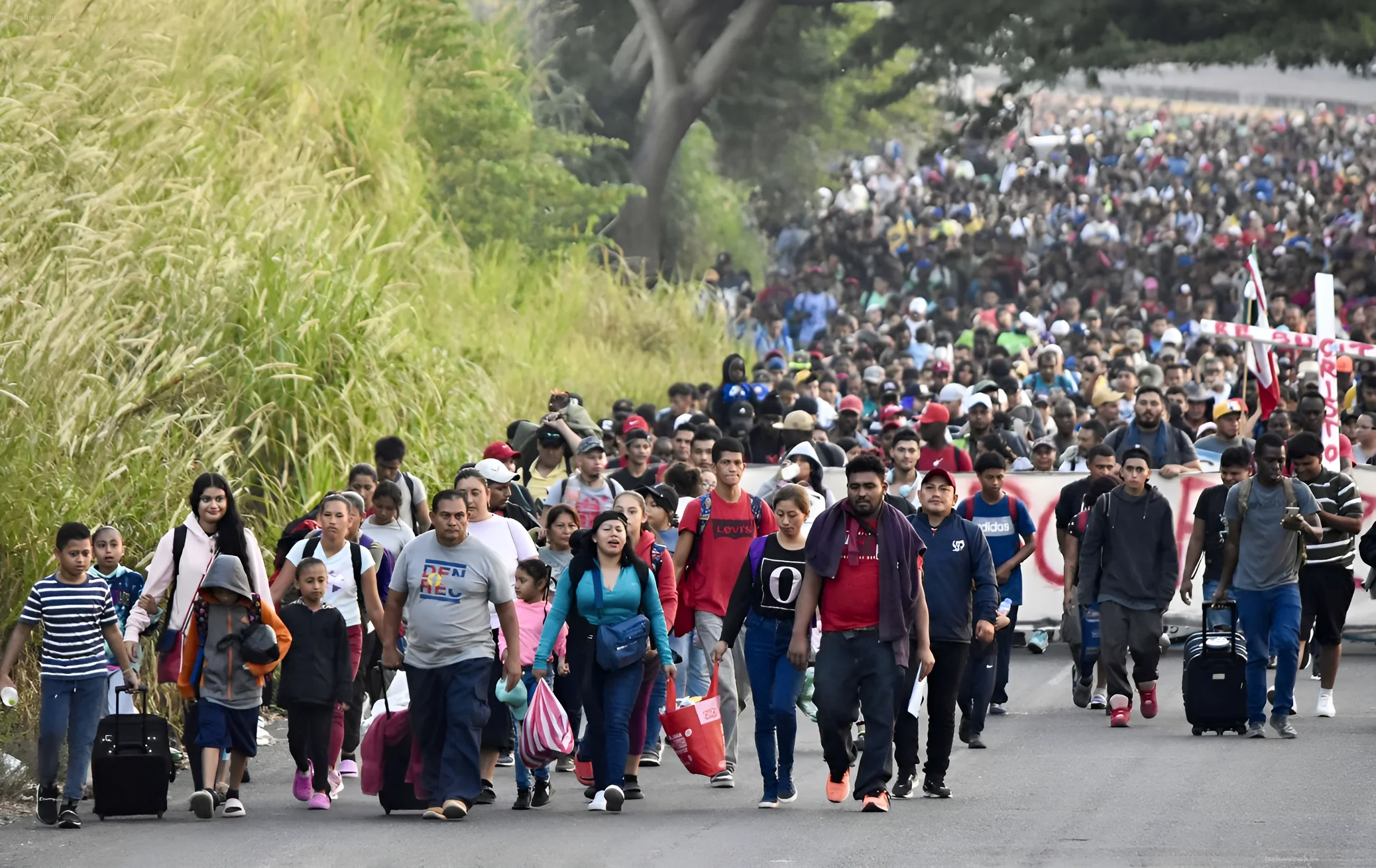 Eine große Gruppe von Menschen mit Koffern und Taschen geht eine Straße entlang, was das Thema Migration und Bevölkerungsbewegung veranschaulicht