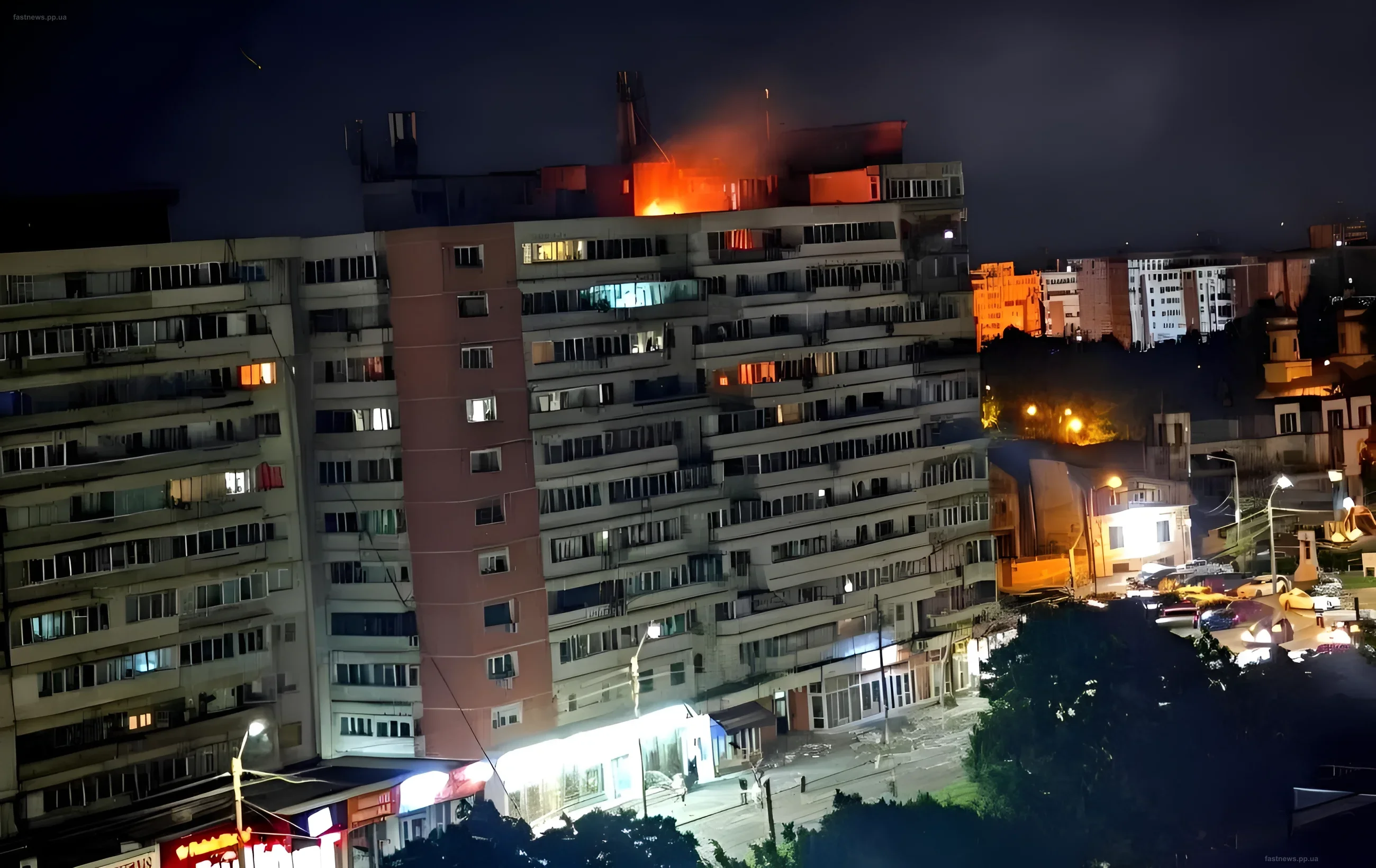 Ночной вид на жилой дом в Галаце, Румыния, после удара российского дрона: огонь на крыше, спасательные работы, уличное освещение и автомобили на фоне темного неба