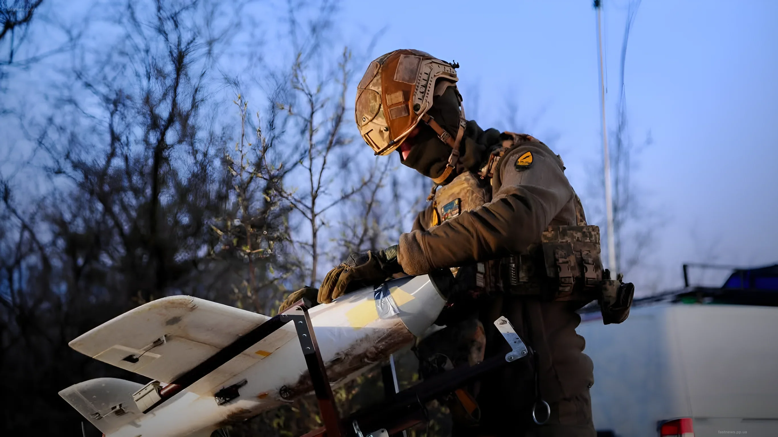 Украинский боец в защитной экипировке готовит к запуску ракету с дрона на фоне деревьев и неба