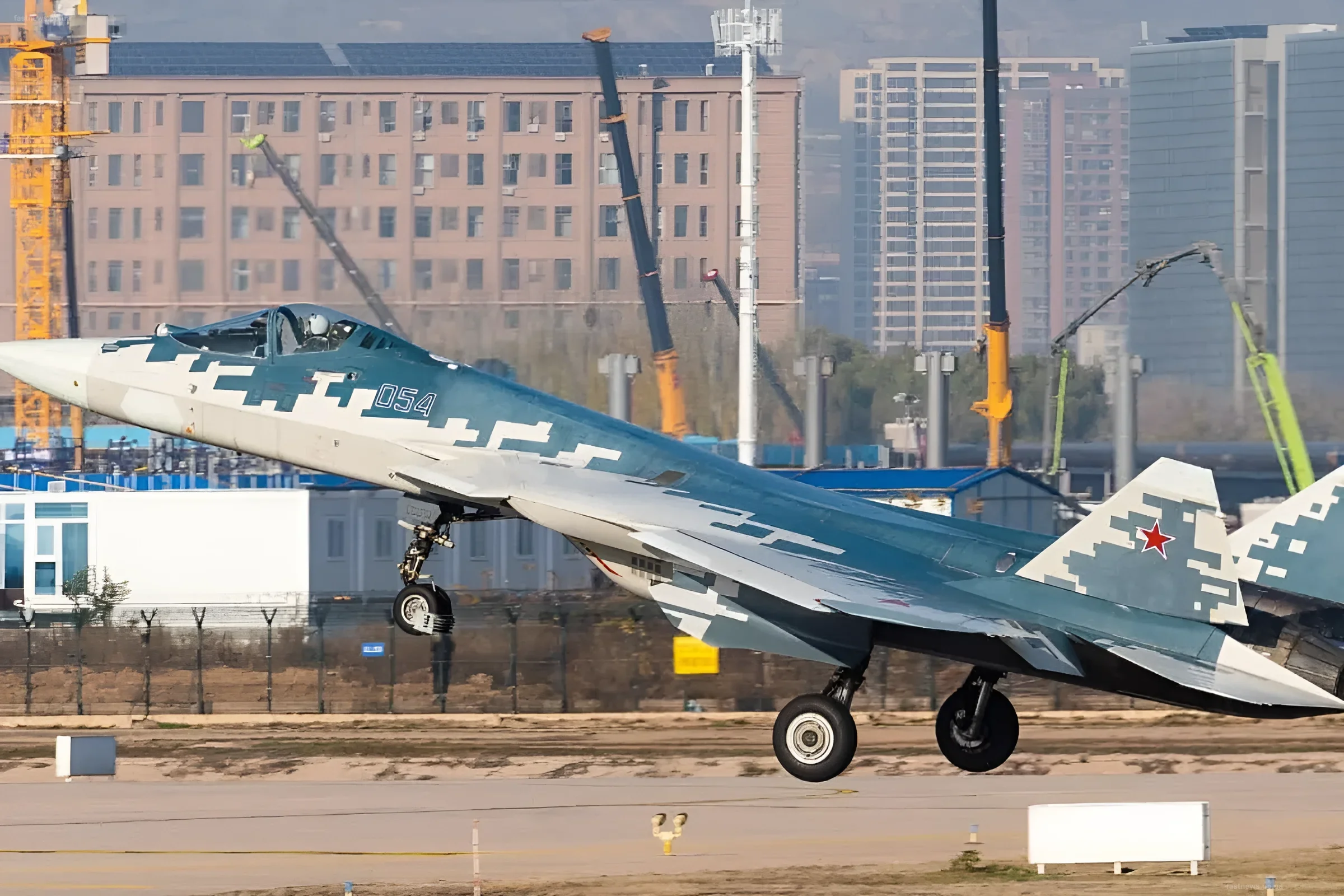 Истребитель Су-57Д в камуфляжной окраске взлетает с полосы на фоне городской застройки