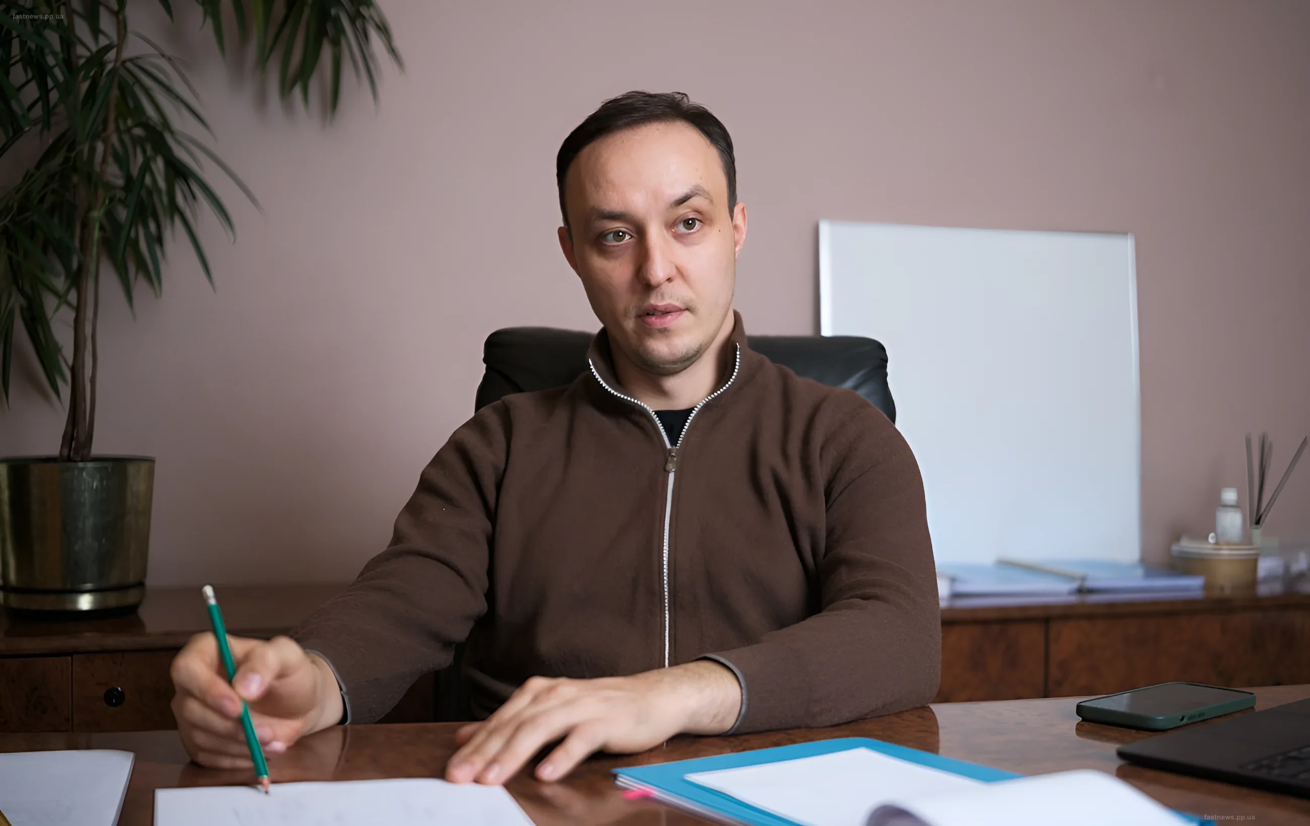 Владислав Власюк за столом с документами и карандашом, демонстрирующий фрагменты ракет и дронов на брифинге