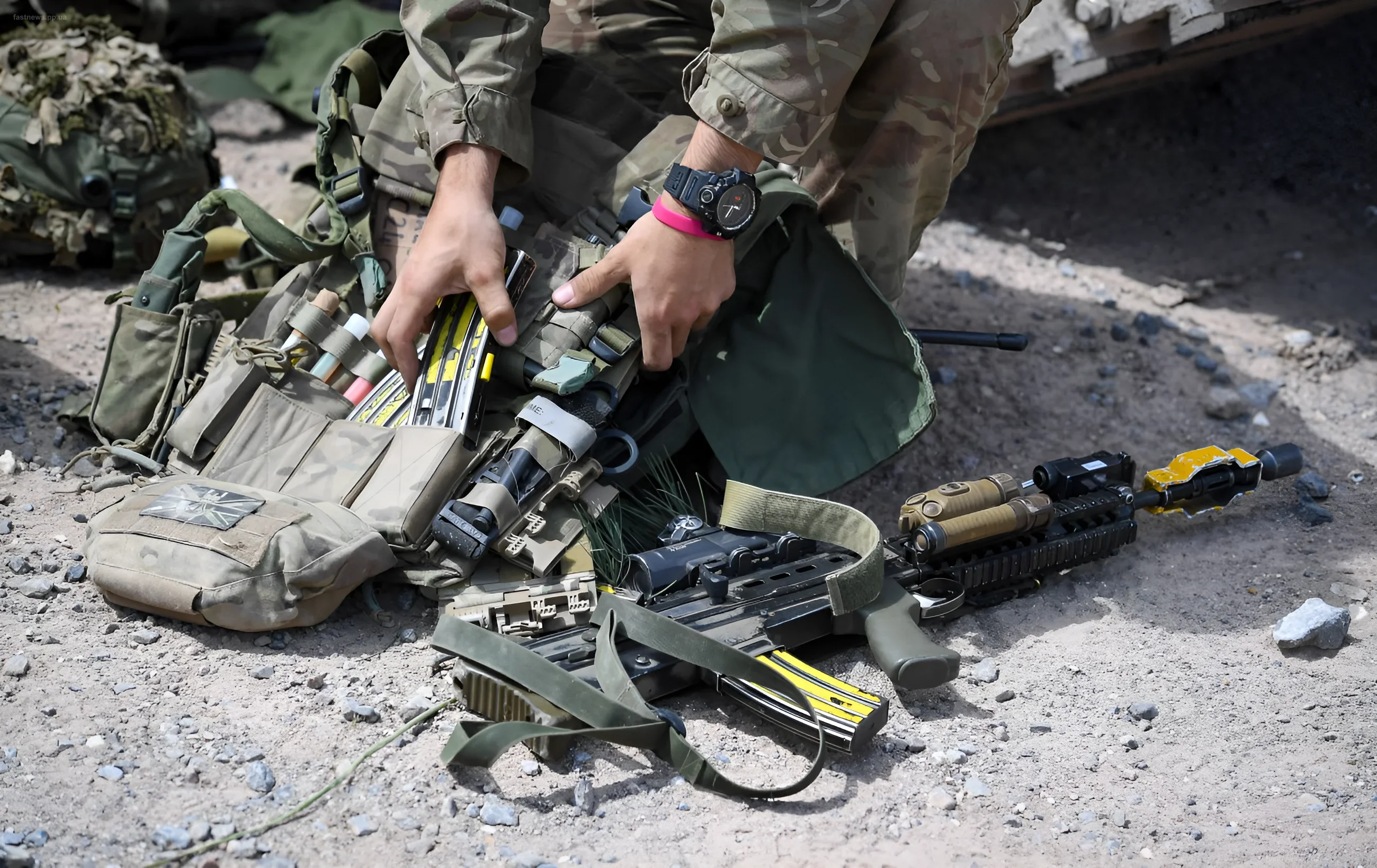 A serviceman in camouflage gear checks equipment and weapons against a desert background
