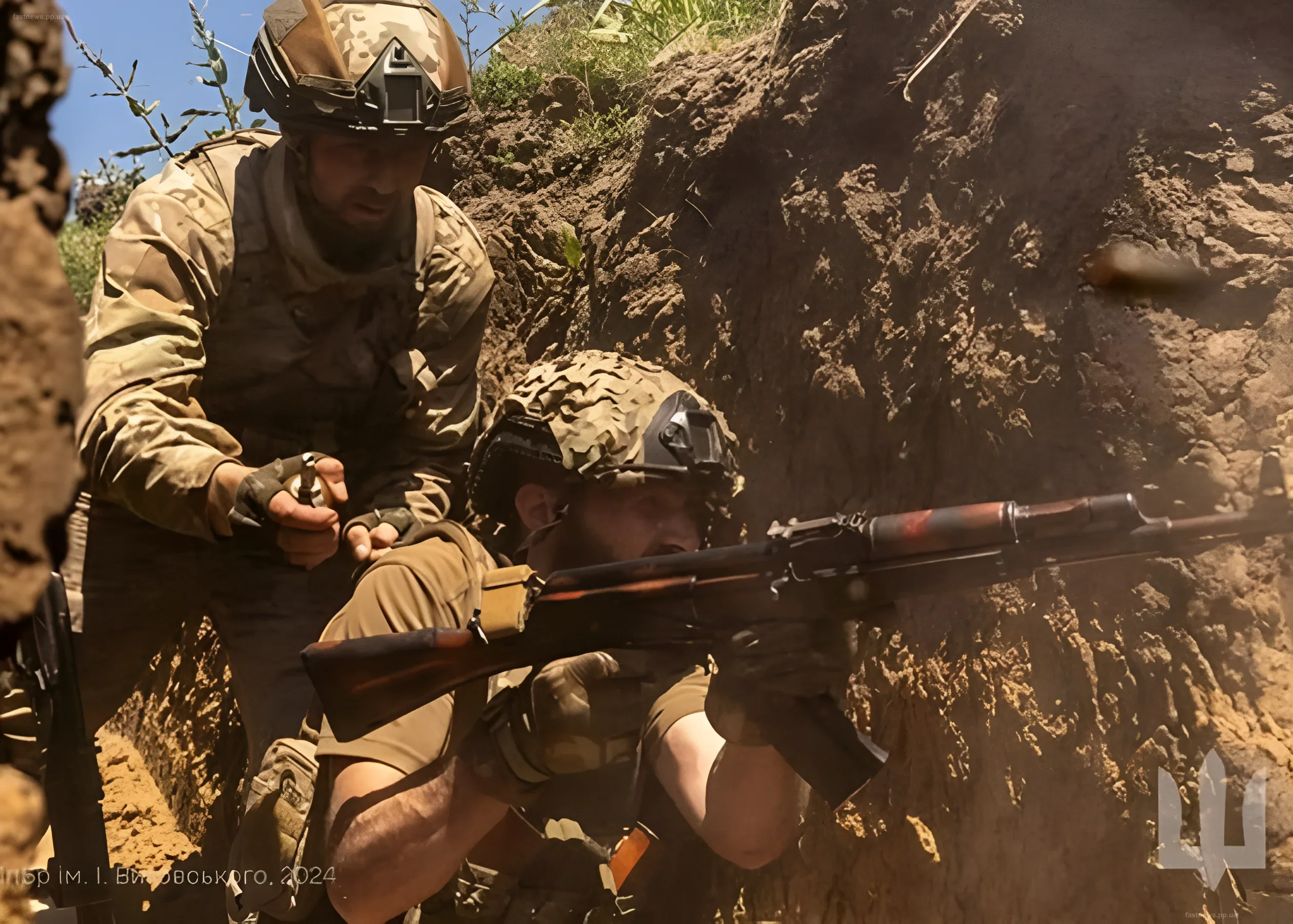 Ukrainian servicemen in full gear observe and cover each other in a trench, with one soldier aiming a sniper rifle.
