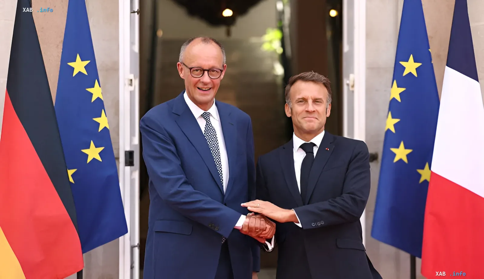 German Chancellor Olaf Scholz and French President Emmanuel Macron shake hands in front of EU, German, and French flags, symbolizing enhanced nuclear cooperation