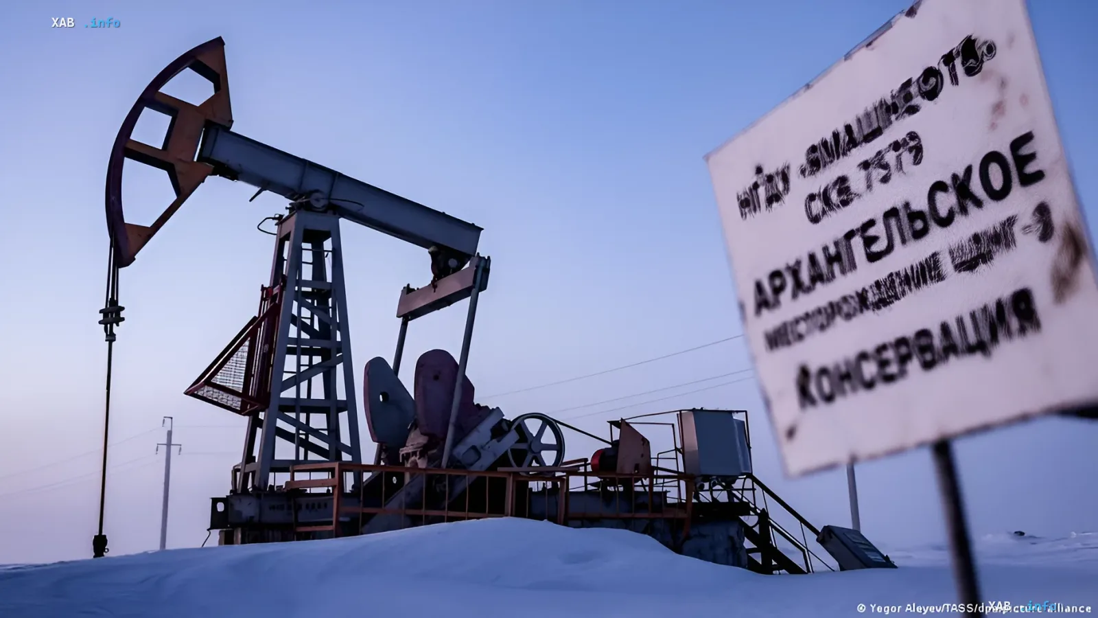 Нефтяная вышка в снежной местности рядом со знаком 'Архангельское месторождение — консервация', иллюстрируя влияние санкций ЕС на российскую нефтяную отрасль