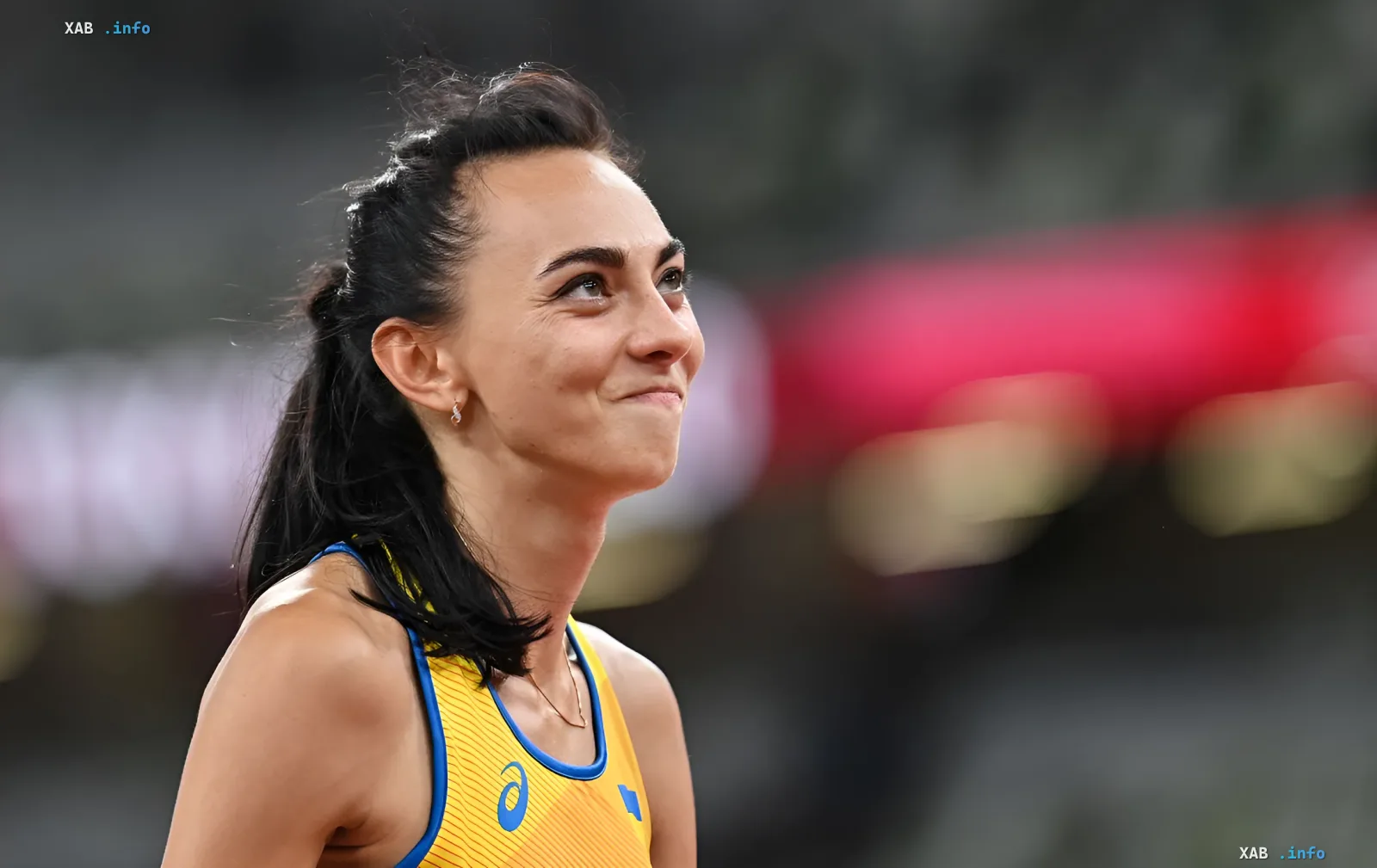 Украинская легкоатлетка Ирина Геращенко в желто-синей форме с логотипом Asics, улыбаясь после победы на стадионе
