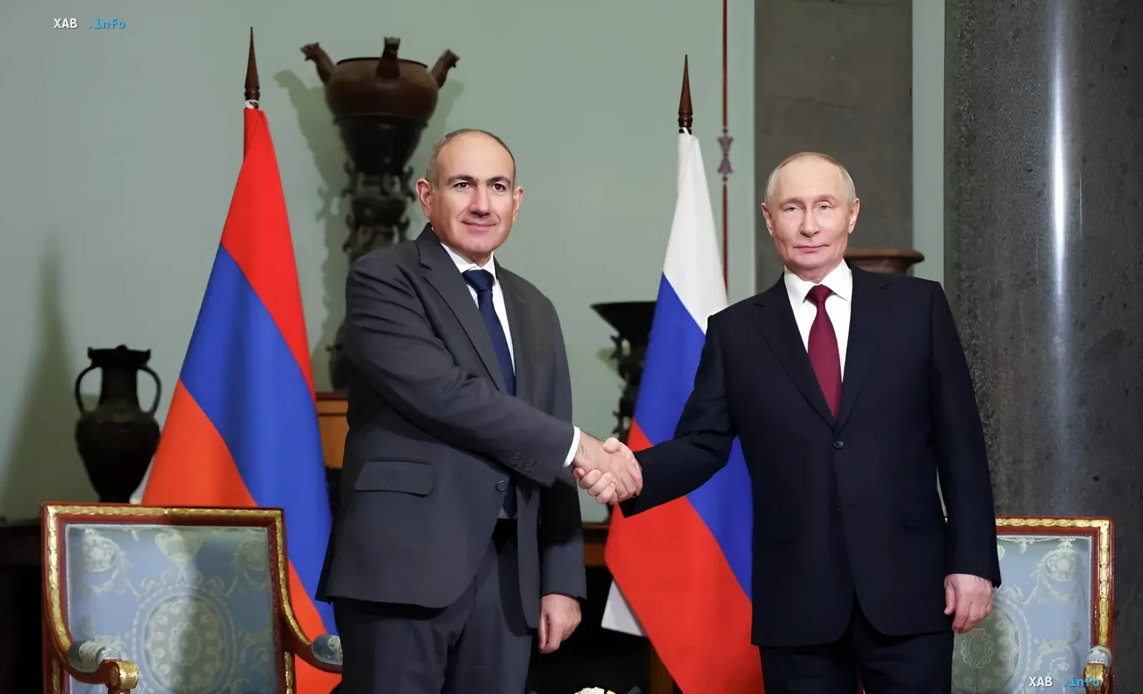 Vladimir Putin and Nikol Pashinyan shake hands in front of Russian and Armenian flags during an official meeting