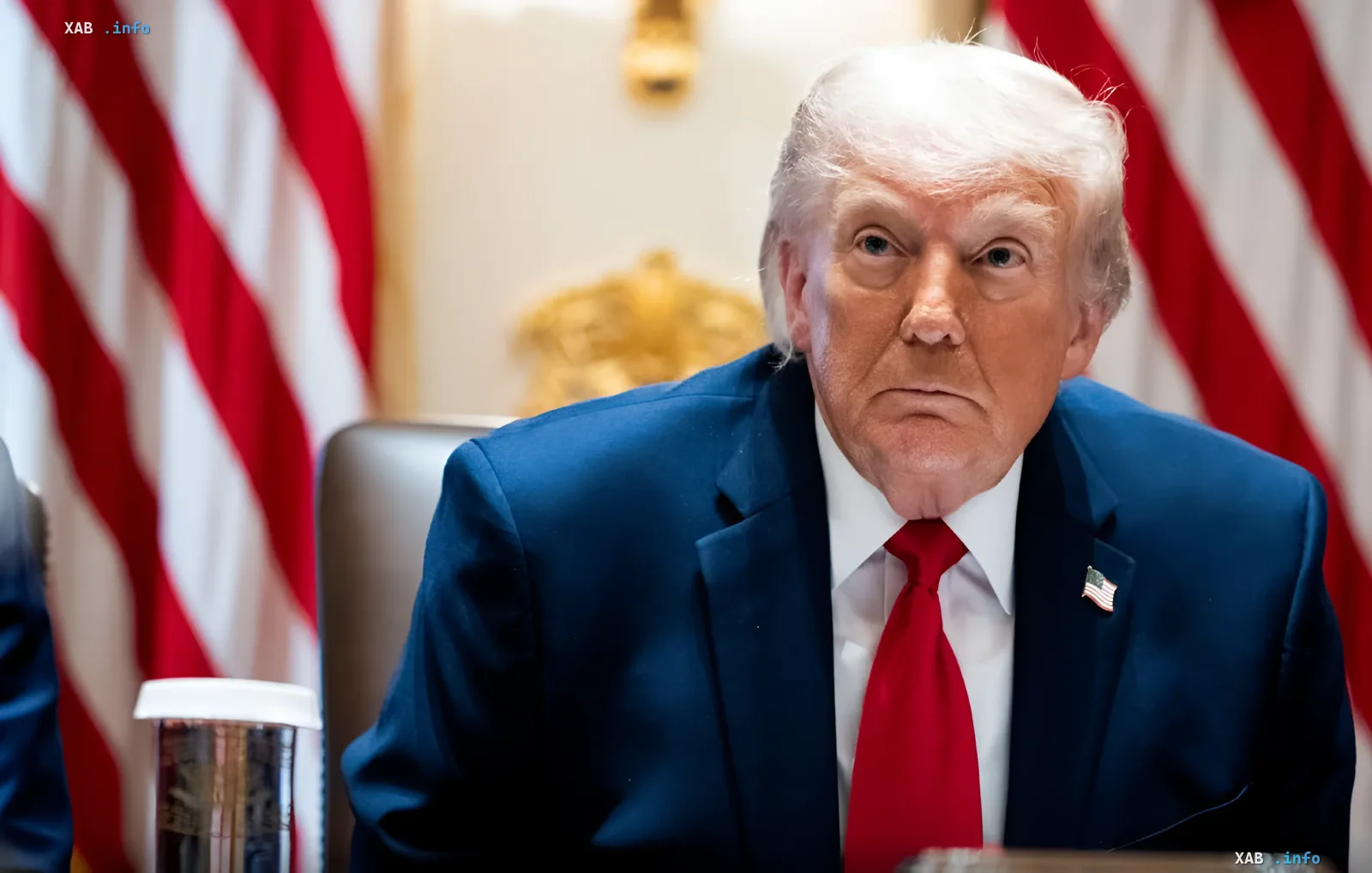 Donald Trump in a blue suit with a serious expression against American flags, illustrating the team's fatigue from Ukraine negotiations