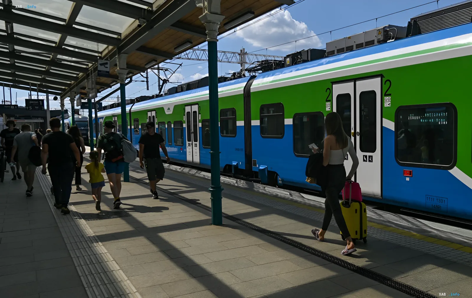 Passagiere mit Gepäck auf einem Bahnhofsumfeld neben einem modernen Zug, der das Thema der direkten Eisenbahnverbindung von Polen zum Flughafen Frankfurt für Ukrainer veranschaulicht