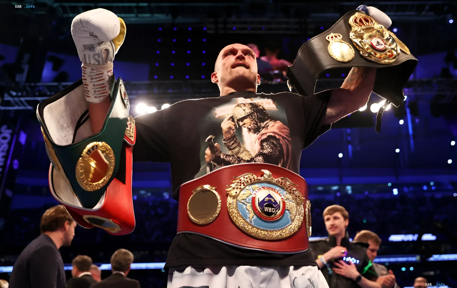 Александр Усик с поясами чемпиона мира в тяжелом весе, включая пояс WBC, на фоне арены после победы