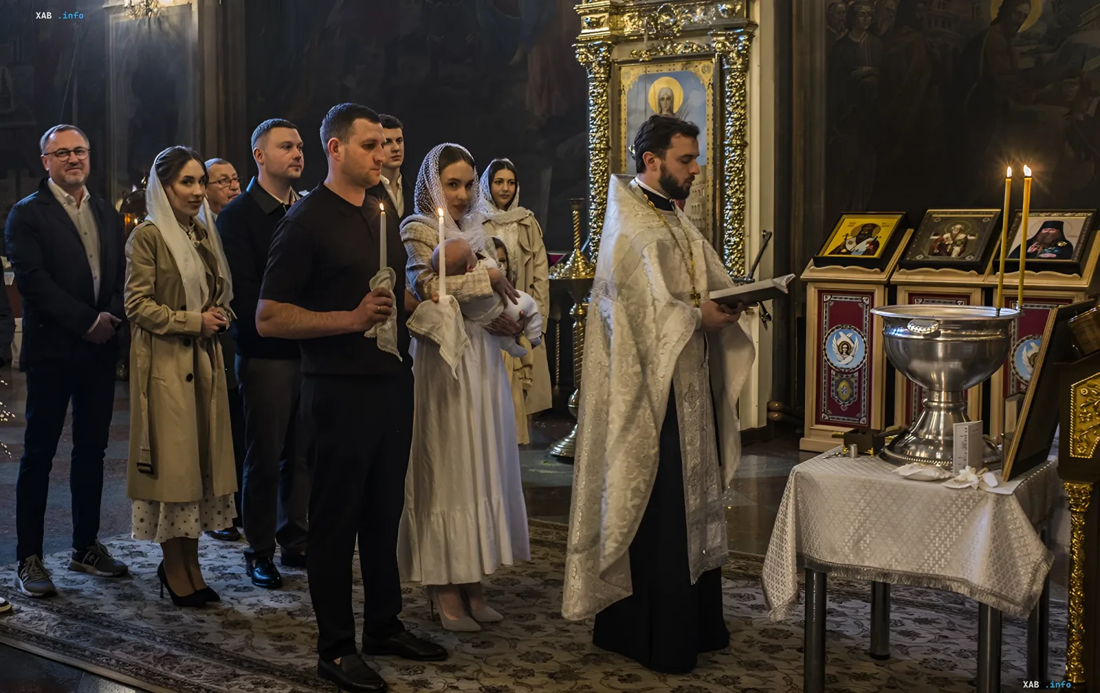 Крещение ребенка в церкви: священник проводит таинство, а крестные родители держат свечи рядом с младенцем