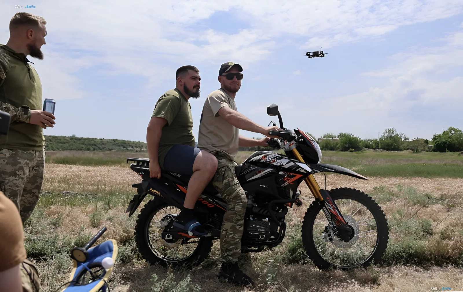Украинские военные на мотоцикле в поле с дроном на фоне, демонстрируя мобильность на фронте