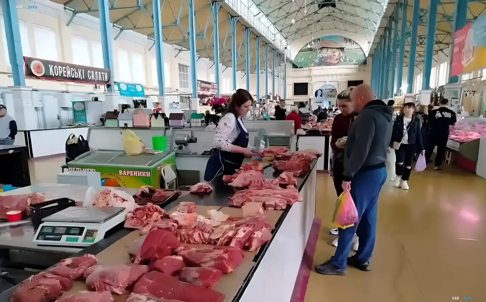 Мясной отдел Нового базара Одессы: цены и ассортимент в начале лета Продавец мяса на Новом базаре в Одессе взвешивает кусок свинины для покупателя, демонстрируя ассортимент мясного отдела в начале лета