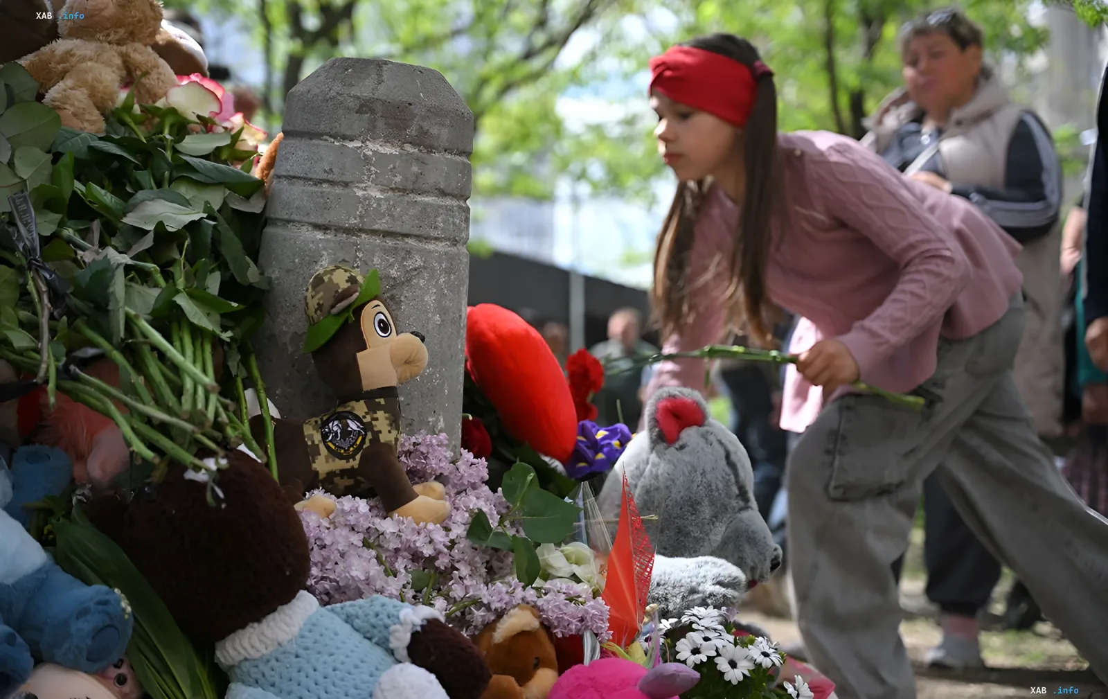 Girl laying flowers at a memorial with stuffed toys on the Day of Remembrance for children killed by Russian aggression