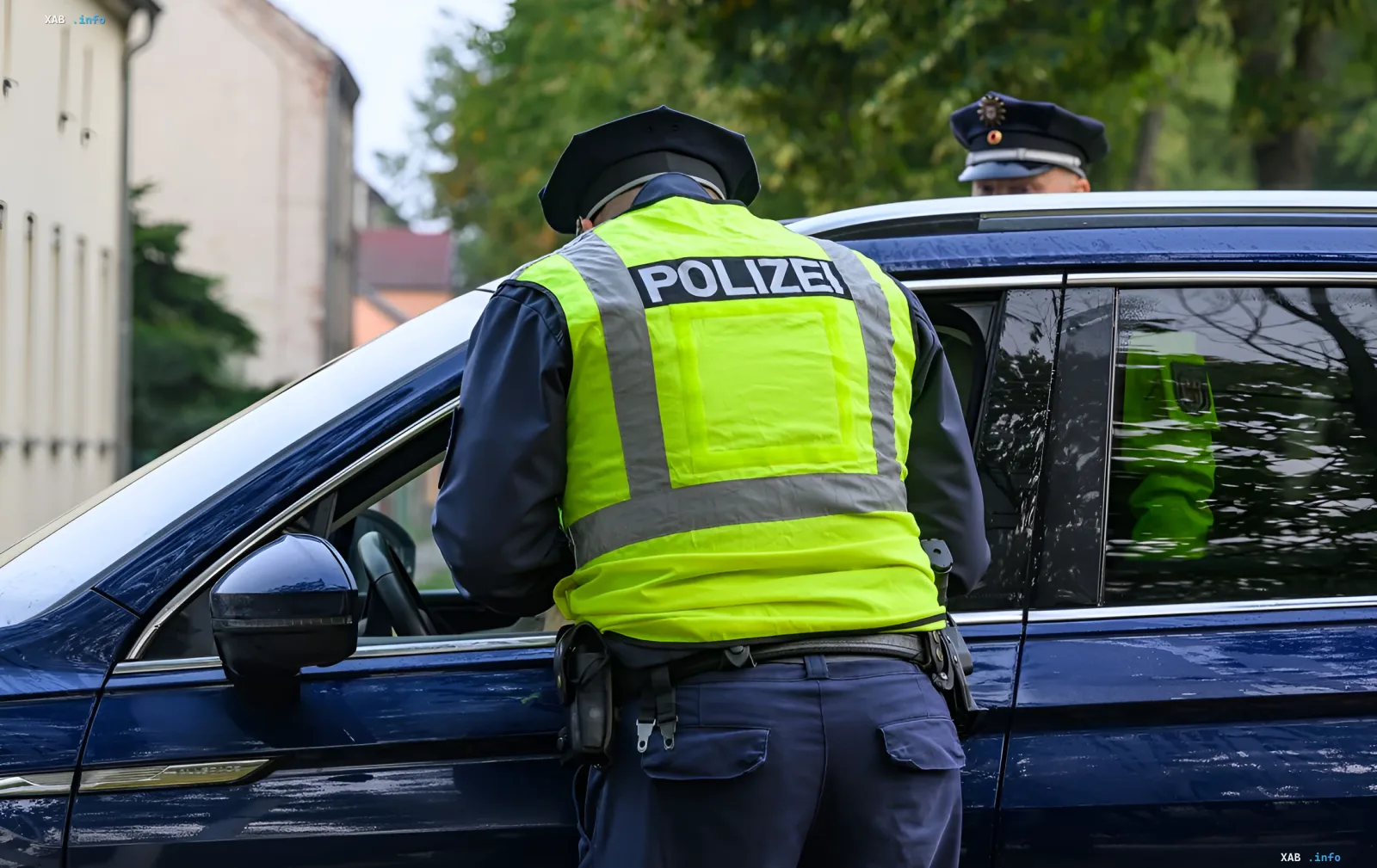 Немецкие полицейские в желтых жилетах с надписью POLIZEI проводят досмотр автомобиля на границе, иллюстрируя сохранение пограничного контроля в Германии