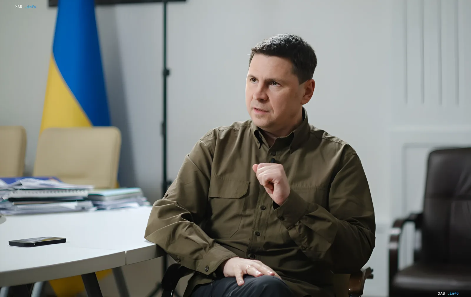 Владимир Зеленский в военной форме, сидящий за столом с украинским флагом на фоне — символ решимости Украины в ответ на угрозы со стороны Беларуси