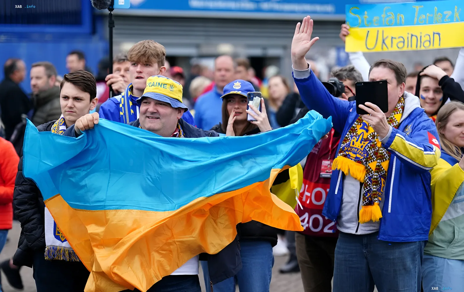 Українські біженці з прапором та шарфами на тлі натовпу, що символізують тему тимчасового захисту в ЄС