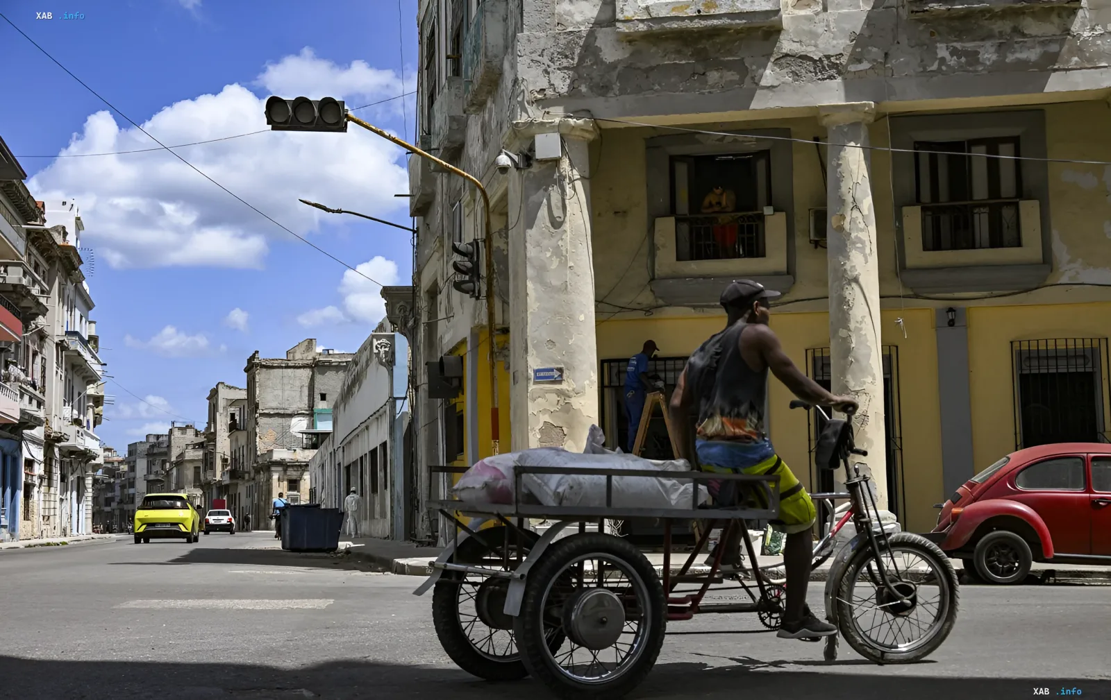 Street in Havana, Cuba: cyclist with a trailer against the backdrop of dilapidated buildings and classic cars, illustrating economic hardships and the exodus of international corporations