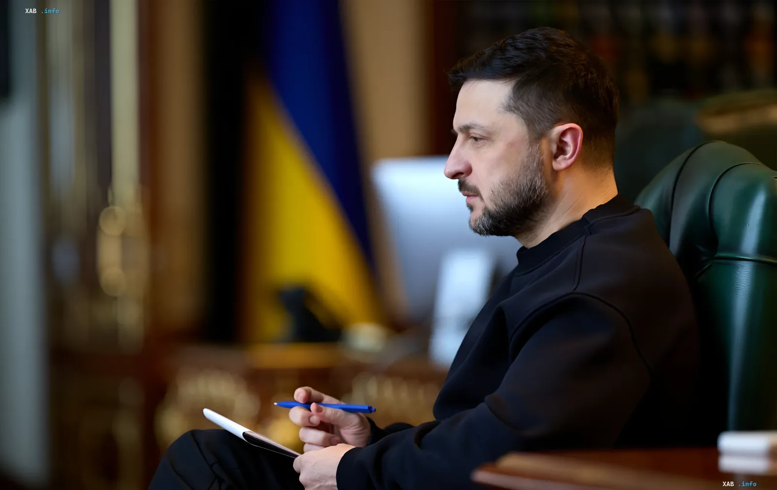 Президент Украины Владимир Зеленский в раздумьях с блокнотом и ручкой на фоне украинского флага — иллюстрация к предложению о заморозке фронта как пути к миру