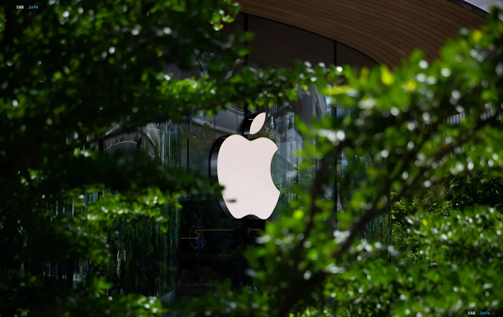 Apple logo on a glass storefront surrounded by lush greenery, symbolizing the seamless integration of Apple Intelligence into daily life with iOS 27
