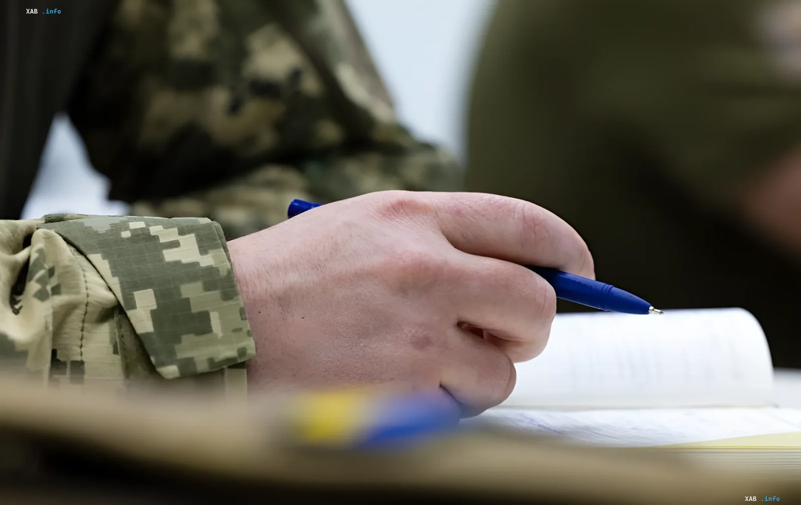 Hand of a soldier in camouflage filling out documents with a blue pen, illustrating the importance of proper documentation for payments