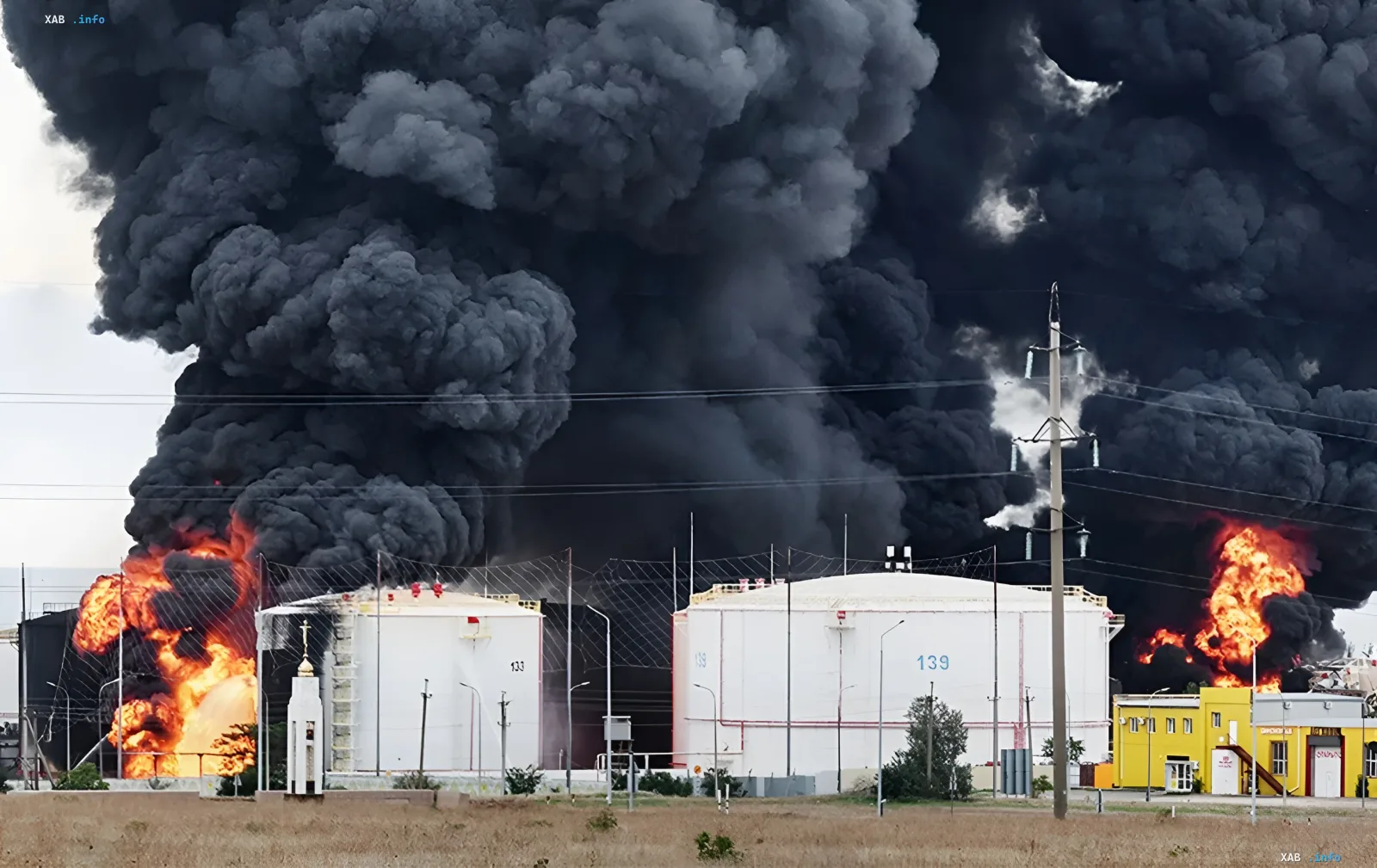 Пожар на нефтеперерабатывающем заводе: огненные столбы и черный дым над резервуарами, иллюстрирующий удары по НПЗ и топливный кризис на юге России