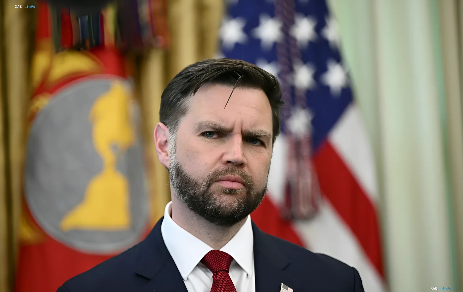 Джей Ди Вэнс в официальном костюме с флагом США на фоне, обсуждающий различия в целях США и Израиля в Иране