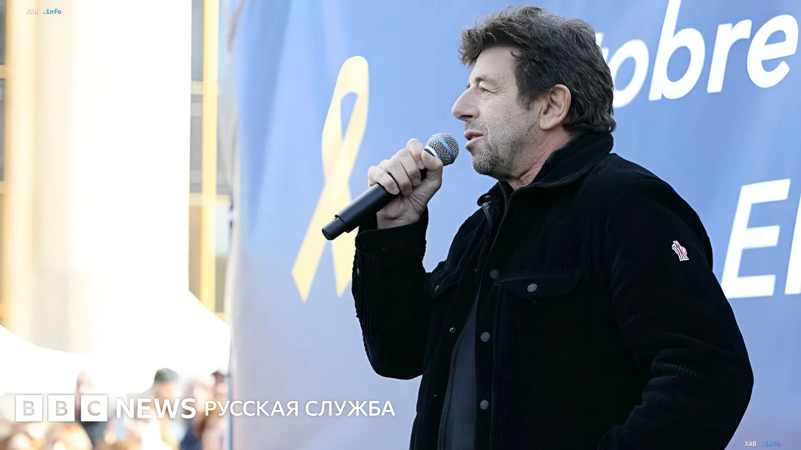 Патрик Брюэль выступает с микрофоном на публичном мероприятии, что контрастирует с новостями о его аресте по обвинениям в сексуальном насилии