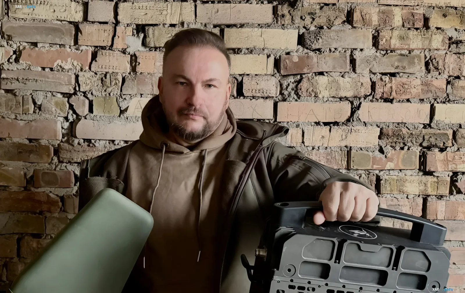 Чоловік з військовою технікою на фоні зруйнованої цегляної стіни — символ наслідків атаки українських ракет «Фламинго» на завод «Прогрес» у Чебоксарах