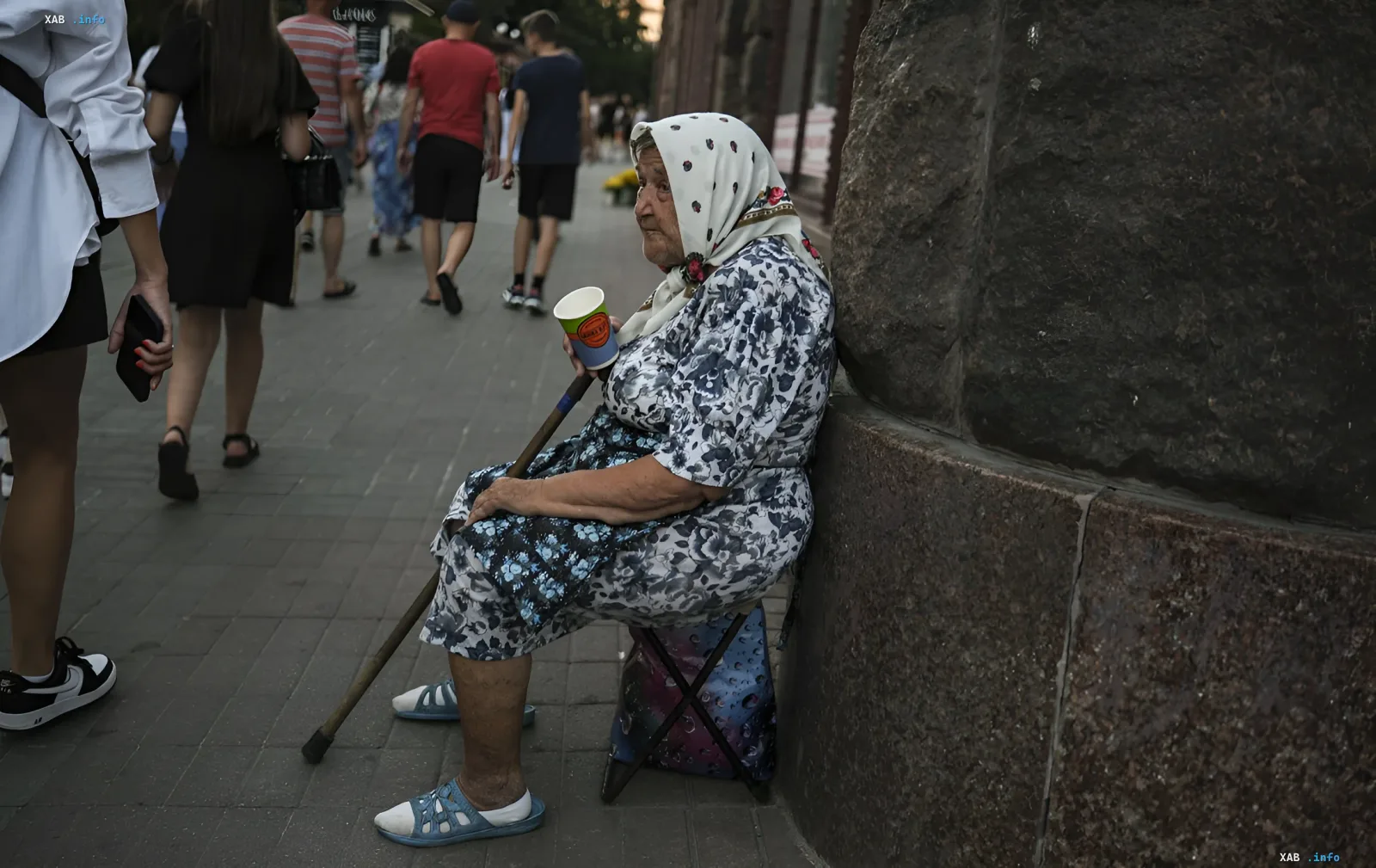 Пенсіонерка сидить на вулиці з чашкою, очікуючи допомоги, ілюструючи тему додаткових виплат до пенсії