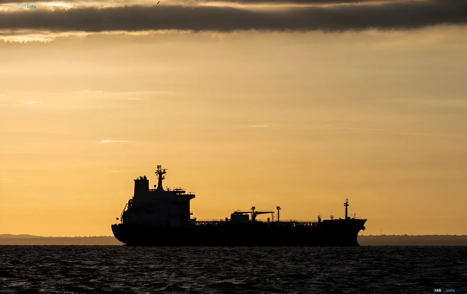 Silhouette eines großen Tankers vor einem Sonnenuntergang im Hormus-Sund, der die Einstellung der Schifffahrt aufgrund der Schließung der strategischen Route durch den Iran symbolisiert