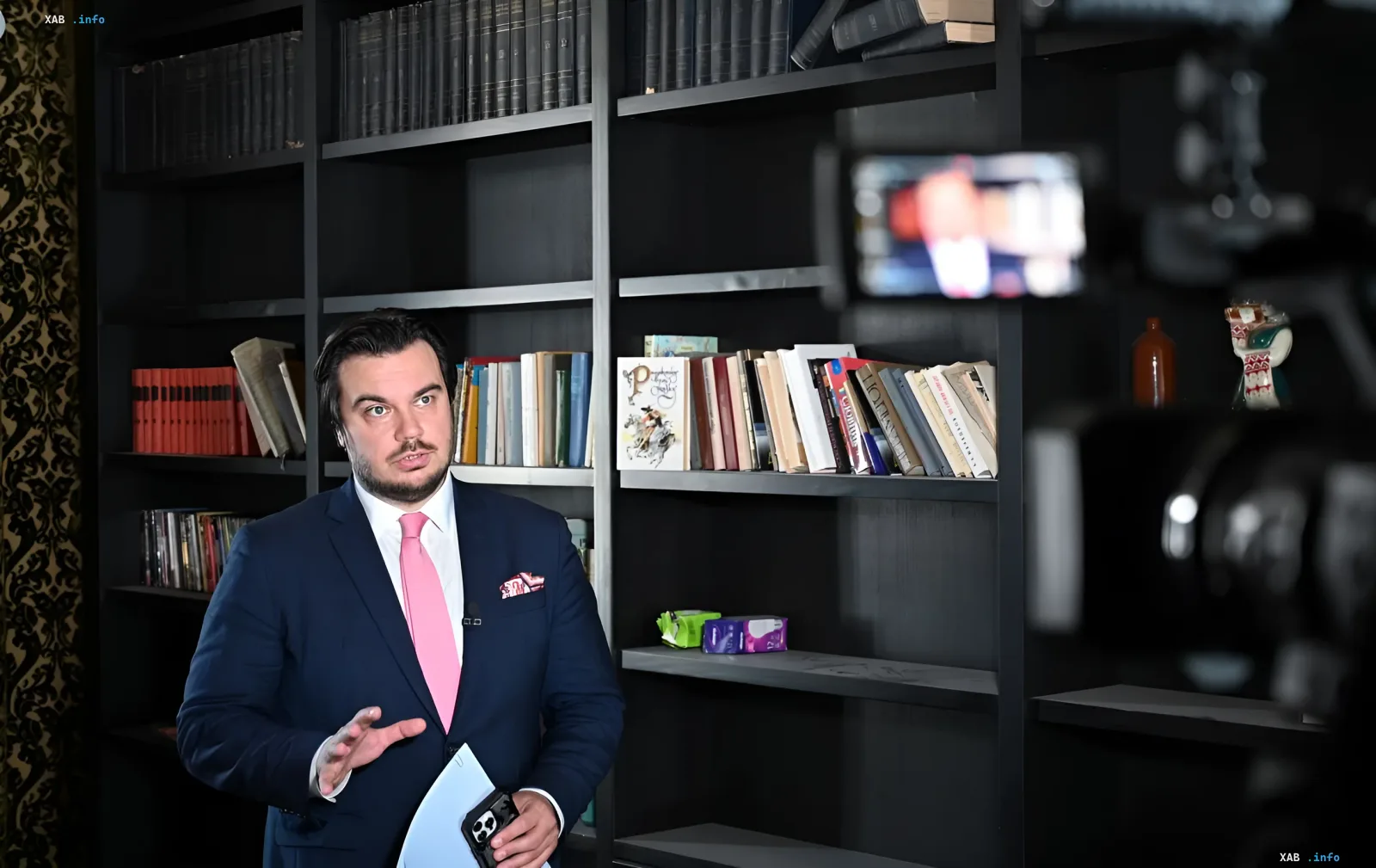 Artemy Lebedev in a suit stands in front of bookshelves in his Kyiv apartment, discussing its fate
