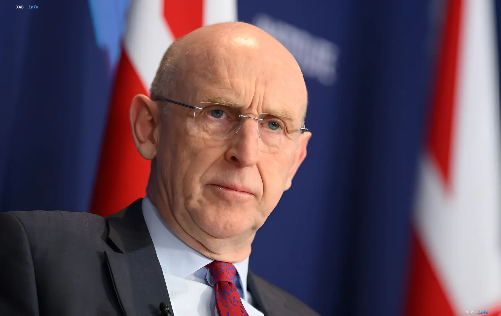 John Healey, britischer Verteidigungsminister, in einer offiziellen Umgebung vor britischen Flaggen, diskutiert Fragen der Unterfinanzierung der Armee