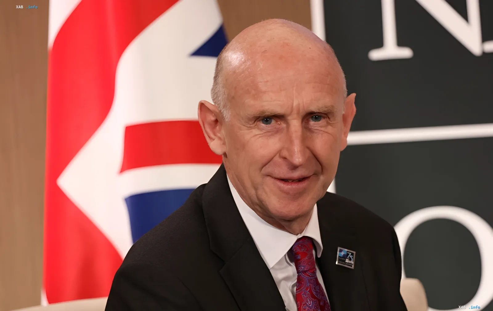 John Gilly, British politician, resigns due to conflict over army funding, in front of the British flag