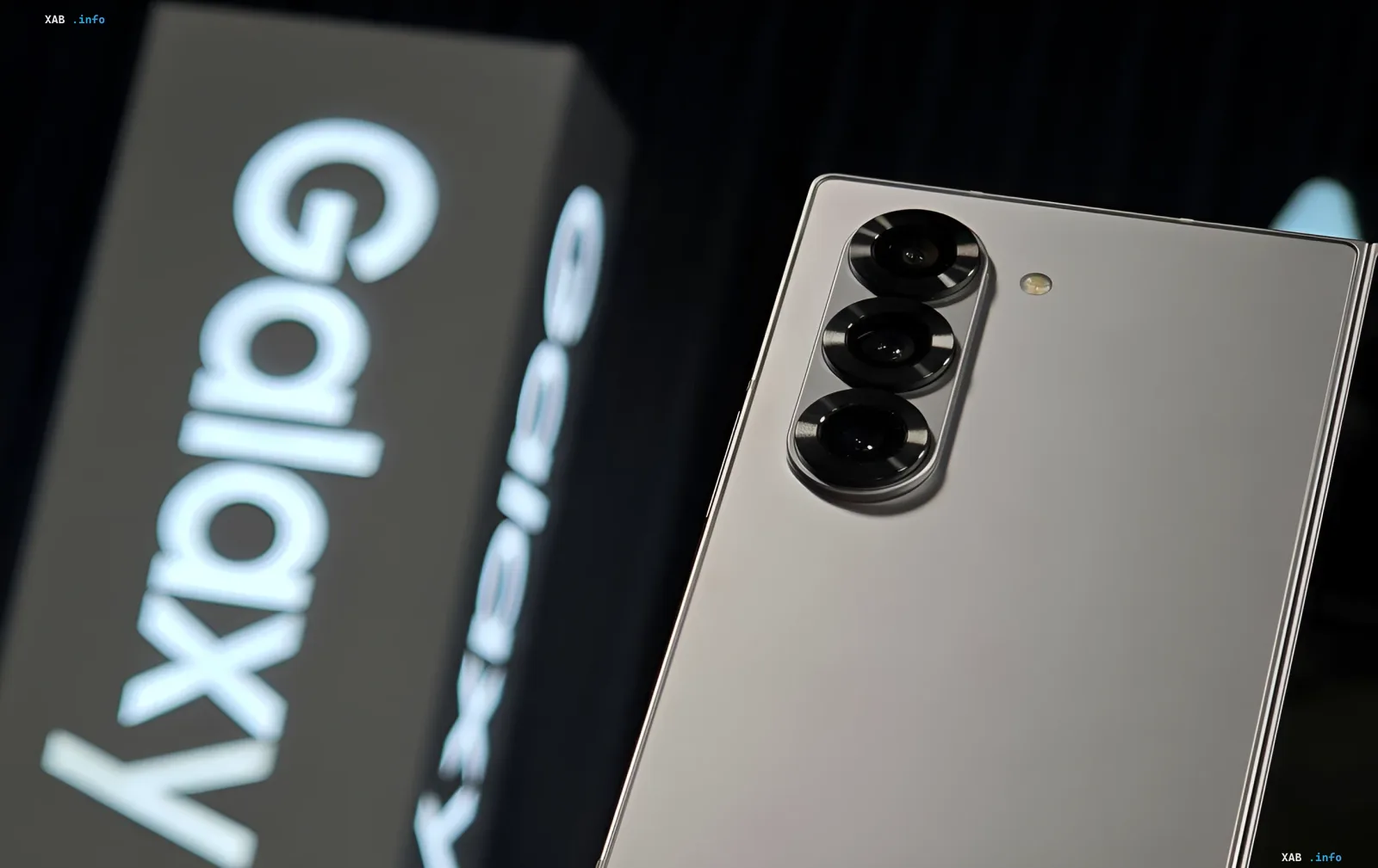 Задняя панель смартфона Samsung Galaxy с тройной камерой на фоне упаковки с надписью Galaxy, иллюстрирующая сравнение флагманских и бюджетных моделей