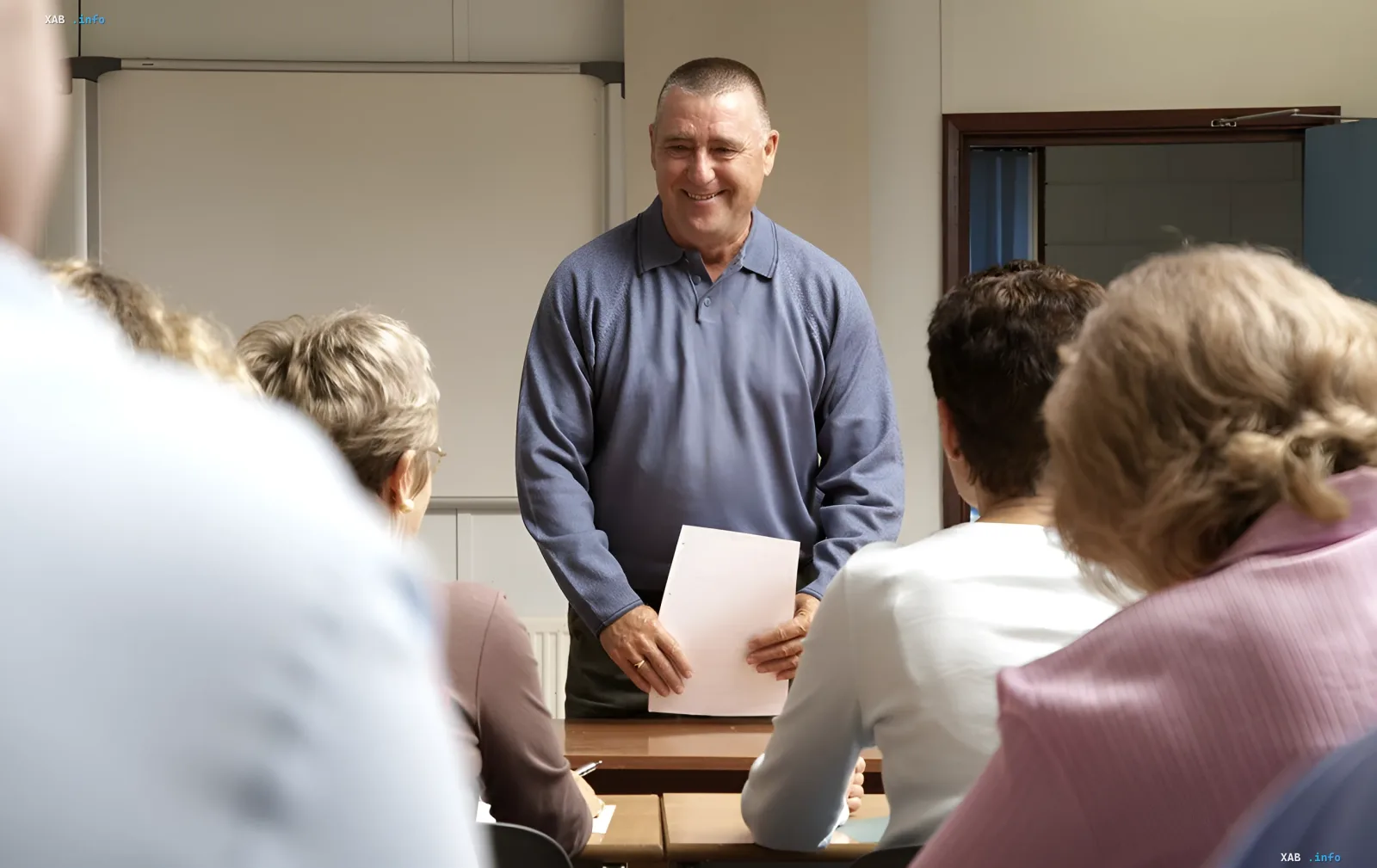 Мужчина-преподаватель с улыбкой держит документ, обращаясь к группе взрослых слушателей в классе — иллюстрация программы переобучения редких профессий в Украине