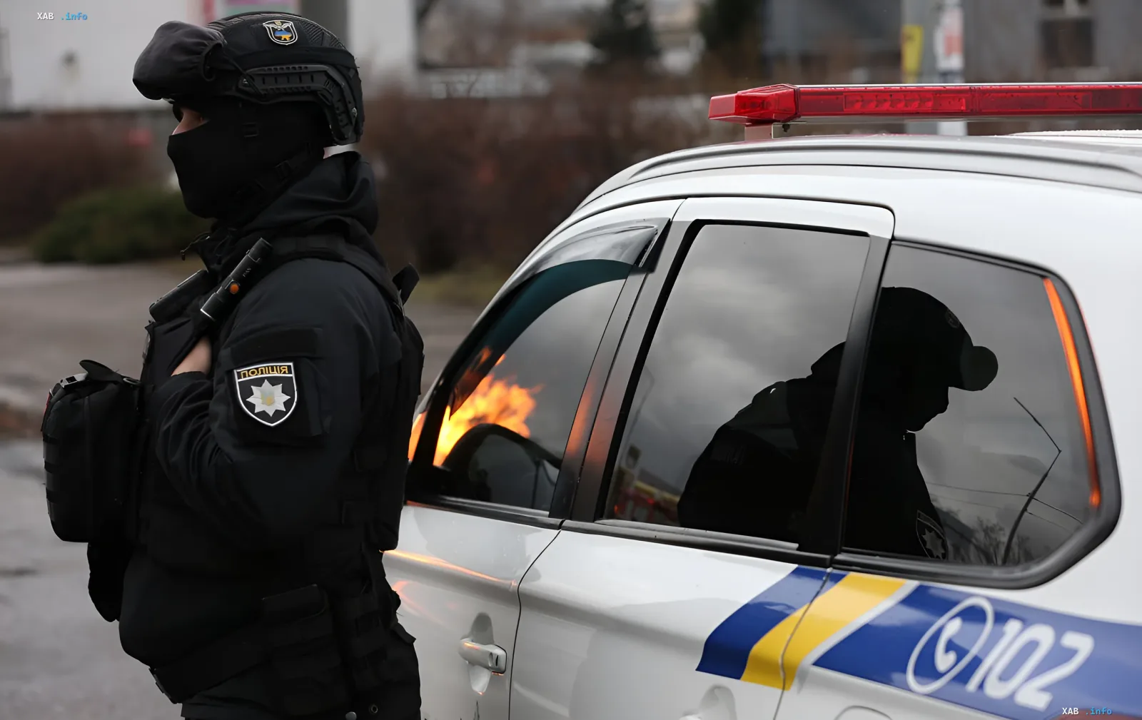 Поліцейський у тактичному спорядженні стоїть поруч із поліцейським автомобілем, у вікні якого відбивається вогонь — ілюстрація до новини про загрозу вибуху в Хусті
