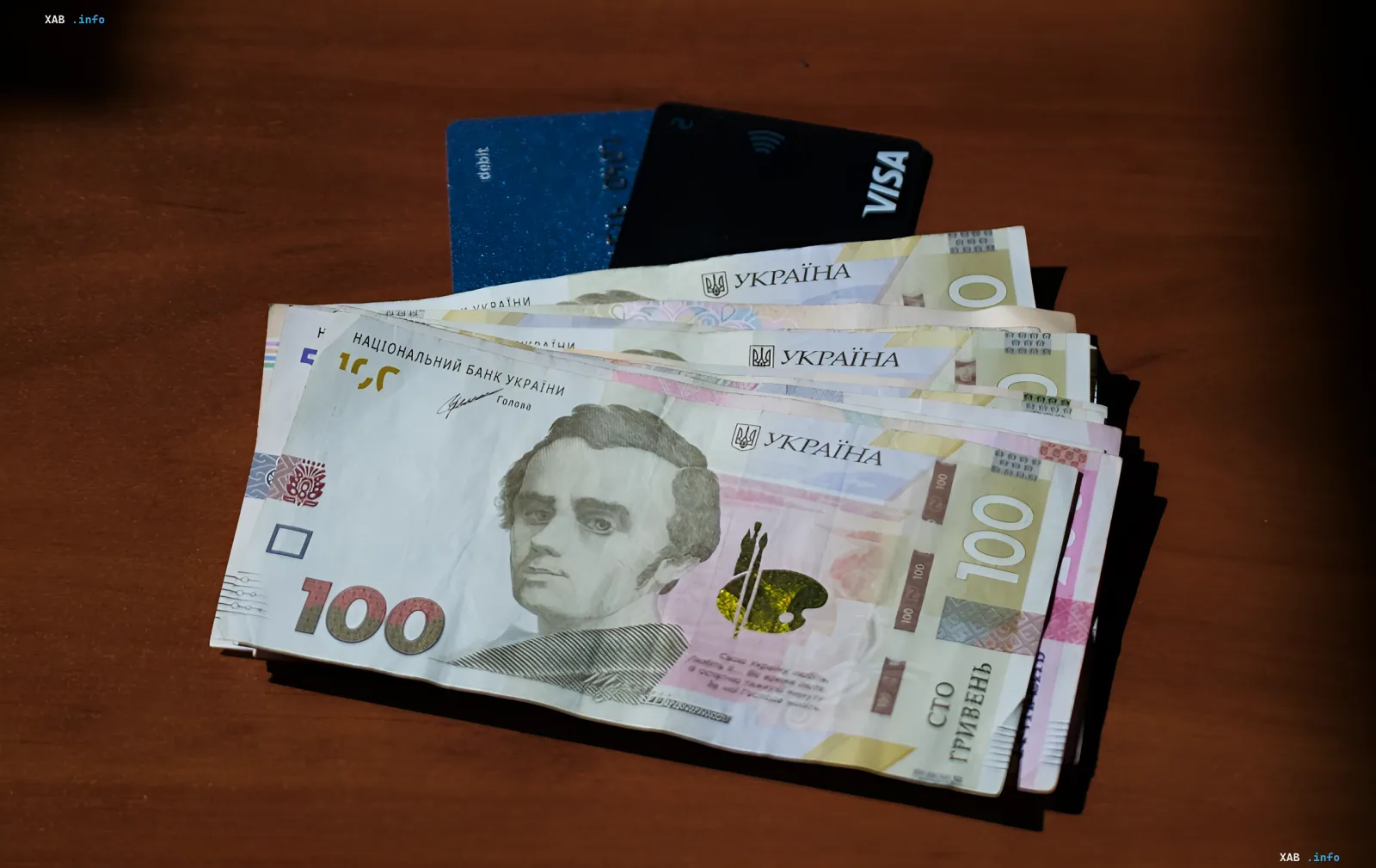 Современные банкноты гривны номиналом 100 гривен с портретом Тараса Шевченко и новые банковские карты, символизирующие обновление платежной системы Украины.