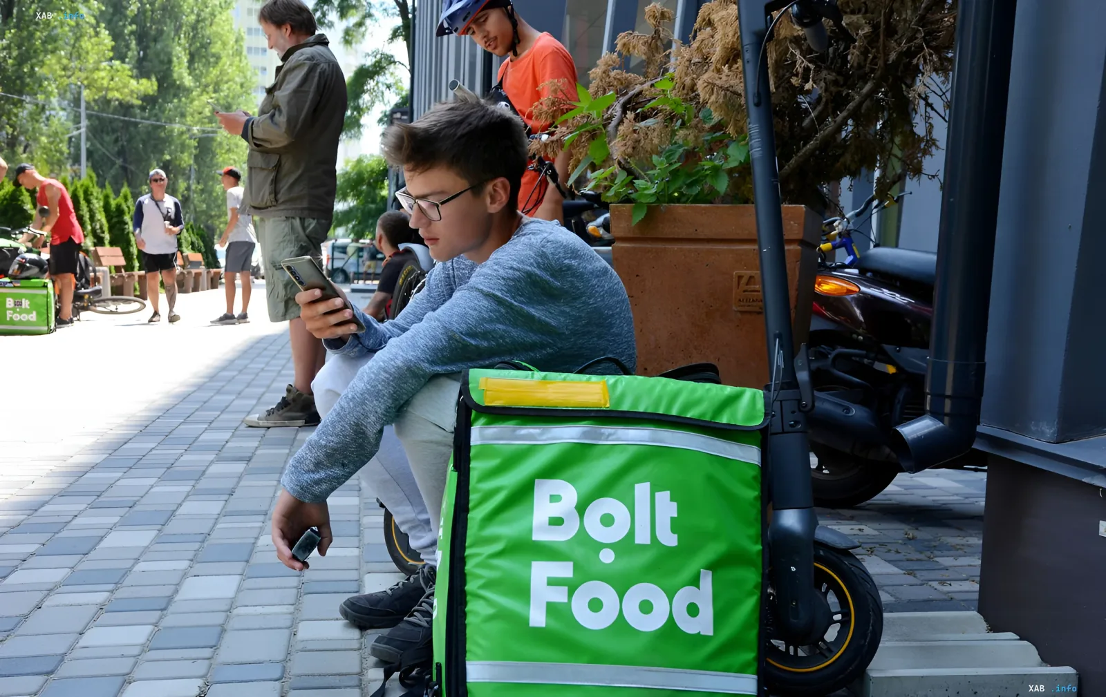 Курьер Bolt Food сидит на тротуаре и проверяет заказы в смартфоне, иллюстрируя работу сервиса доставки в условиях кадрового дефицита в Украине.