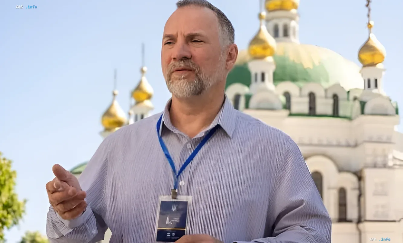 Мужчина с бородой в синей рубашке и бейджем на фоне золотых куполов Киево-Печерской Лавры, обсуждающий вопрос о прахе Столыпина