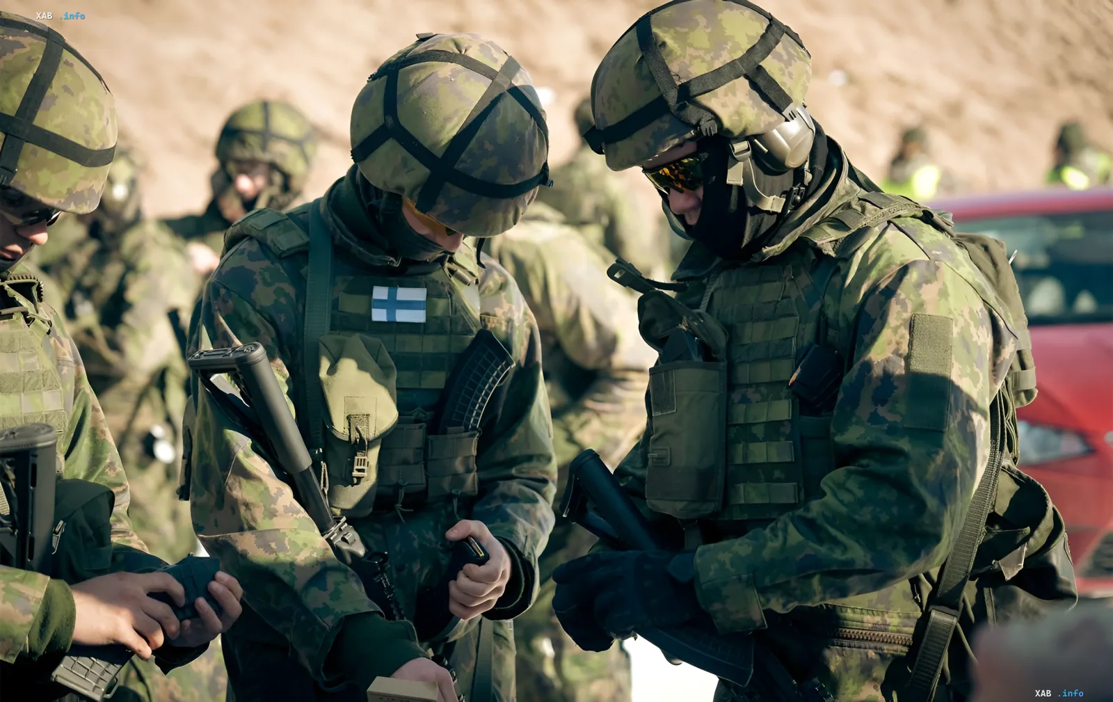 Финские военнослужащие в камуфляже с флагом Финляндии на жилете обсуждают тактику на фоне военной техники