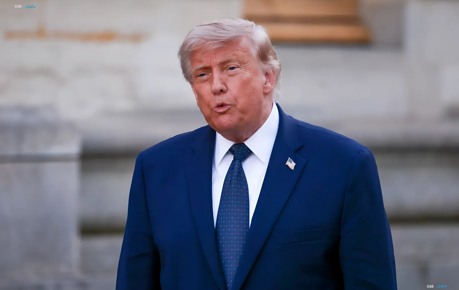 Дональд Трамп в синем костюме с американским флагом на лацкане, обсуждающий договоренность с Ираном