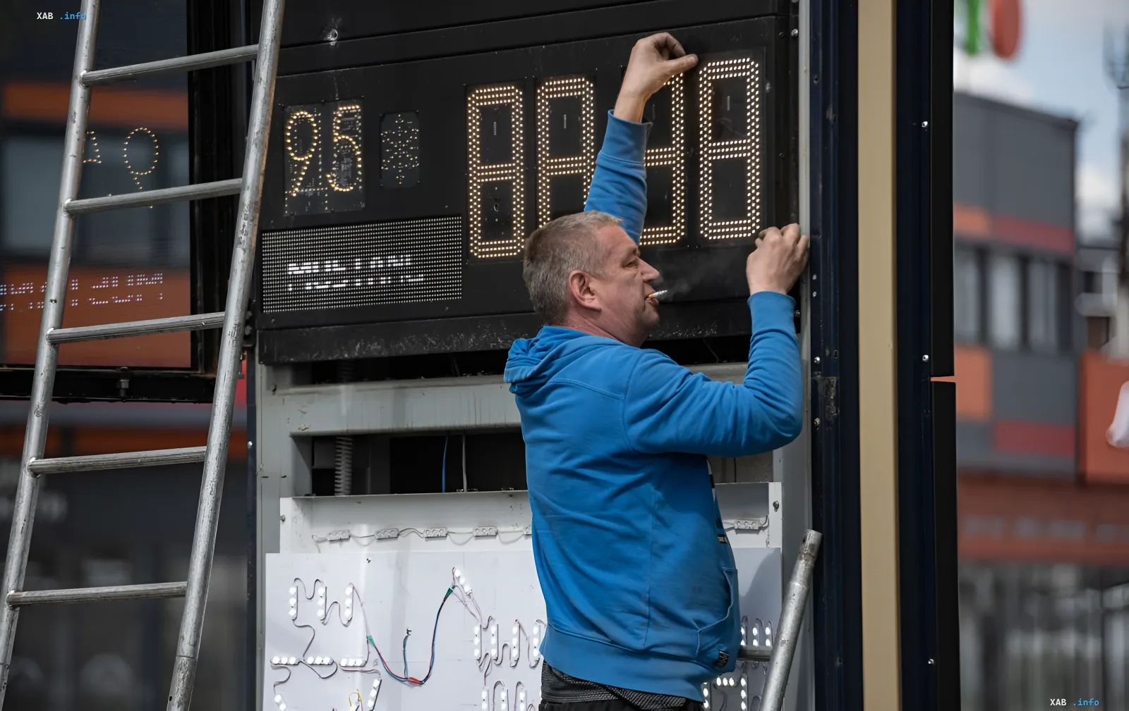 Worker repairing broken fuel price display at gas station — symbol of hidden fuel collapse in Russia