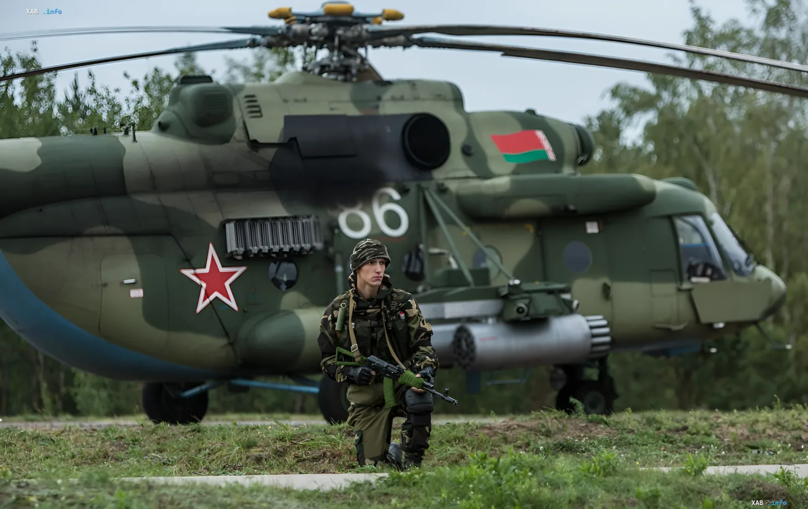 Белорусский военный в камуфляже с автоматом на фоне вертолёта Ми-8 с флагом Беларуси и красной звездой — символ мобилизационных учений у границы НАТО
