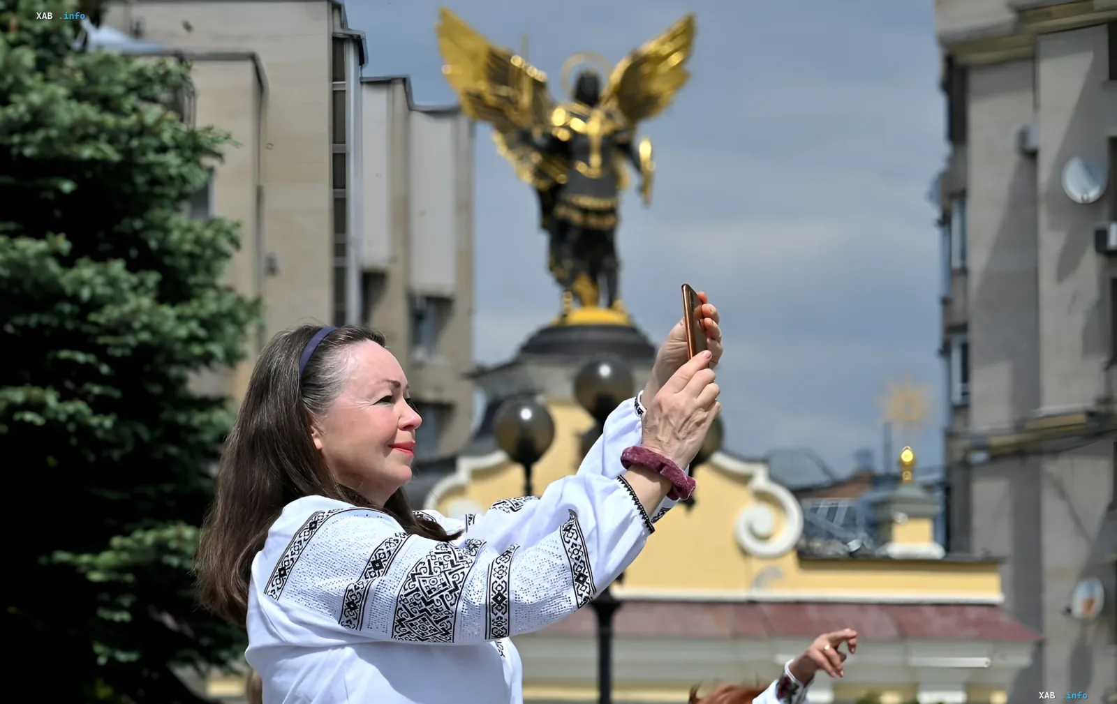 Woman in vyshyvanka photographing the Archangel Michael monument against clear sky — illustration for forecast of heat up to +32°C and thunderstorms in Ukraine