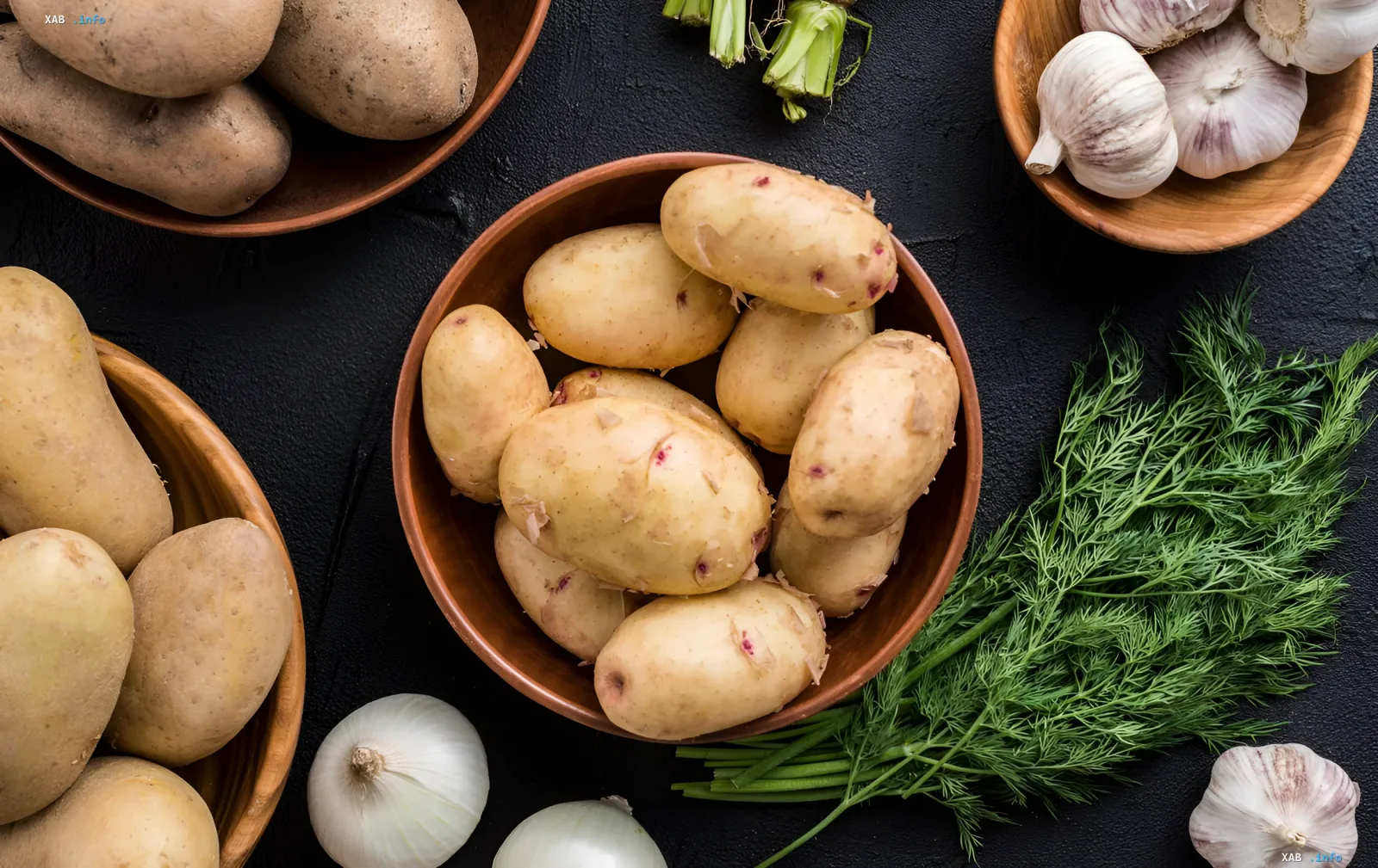 Fresh young potatoes in wooden bowls with onions, garlic, and dill on a dark background, illustrating the drop in prices for the harvest in Ukraine
